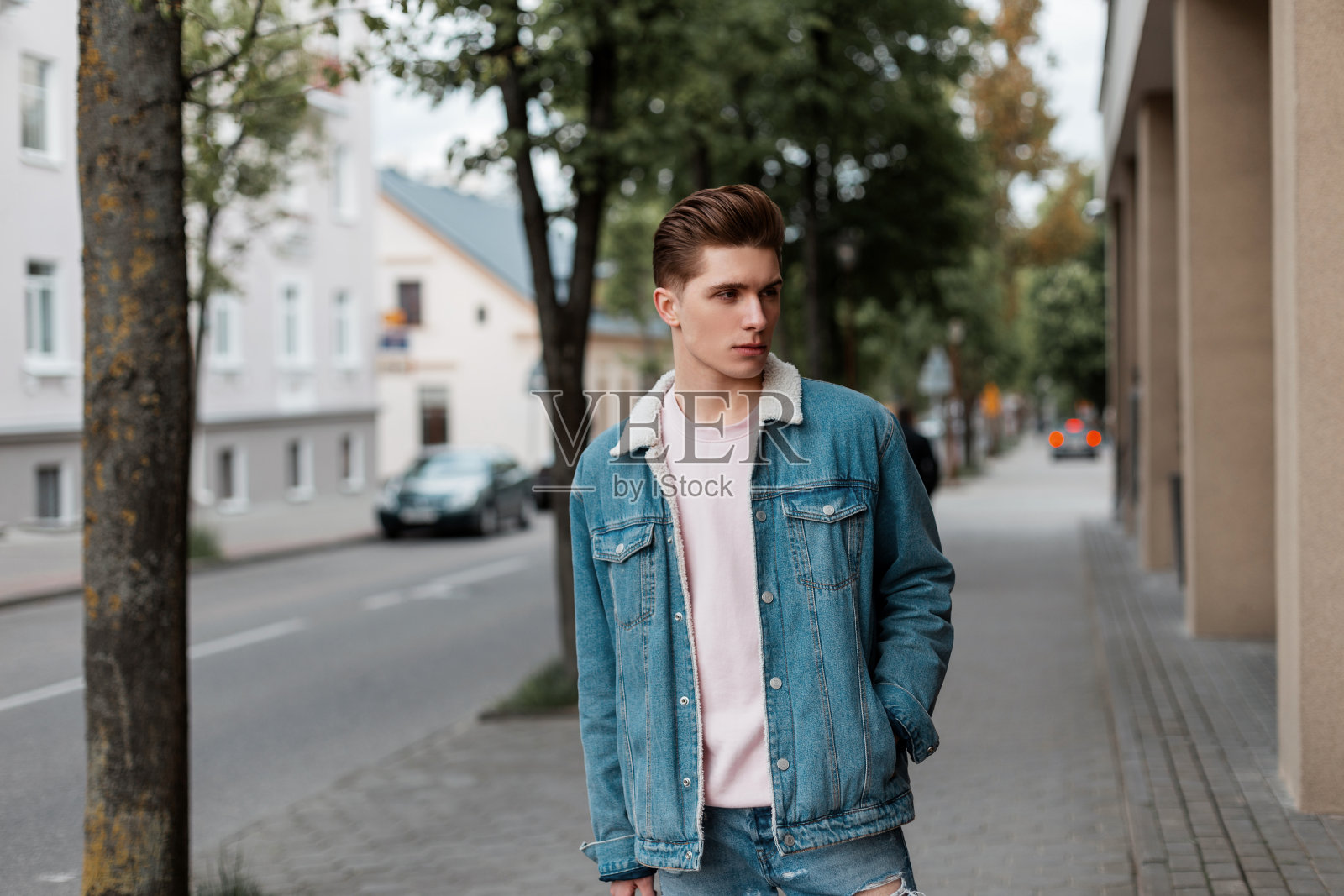 漂亮时髦的年轻人，发型粉红色的t恤，时髦的蓝色青年休闲牛仔裤衣服走在街道附近的道路。穿着时髦衣服的帅哥在城市里旅行。时尚的夏季男装。照片摄影图片