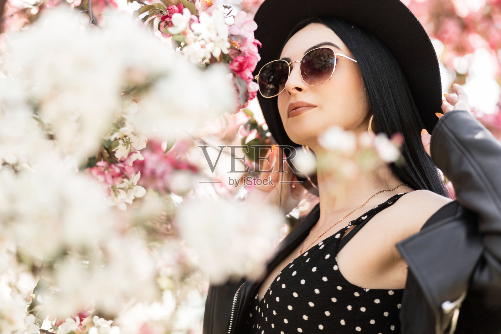 美女肖像时尚美丽的年轻女子在时尚太阳镜在优雅的帽子在时尚的春天黑色衣服在公园附近惊人的花朵。漂亮漂亮的女孩在大自然中散步。良好的休息。照片摄影图片