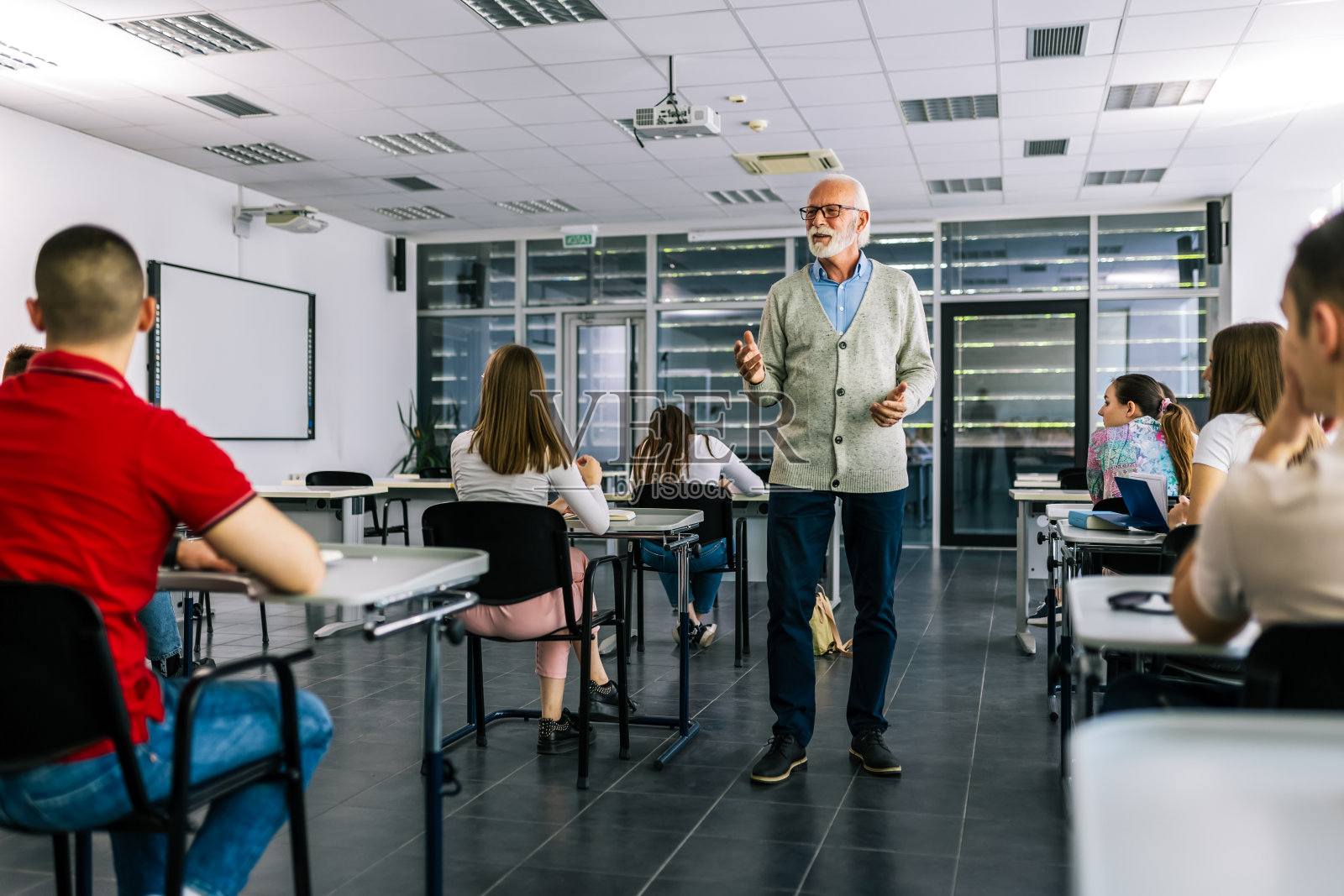 一群学生在上课时拿着书。学生们正在听一位年长的高中老师讲课。照片摄影图片
