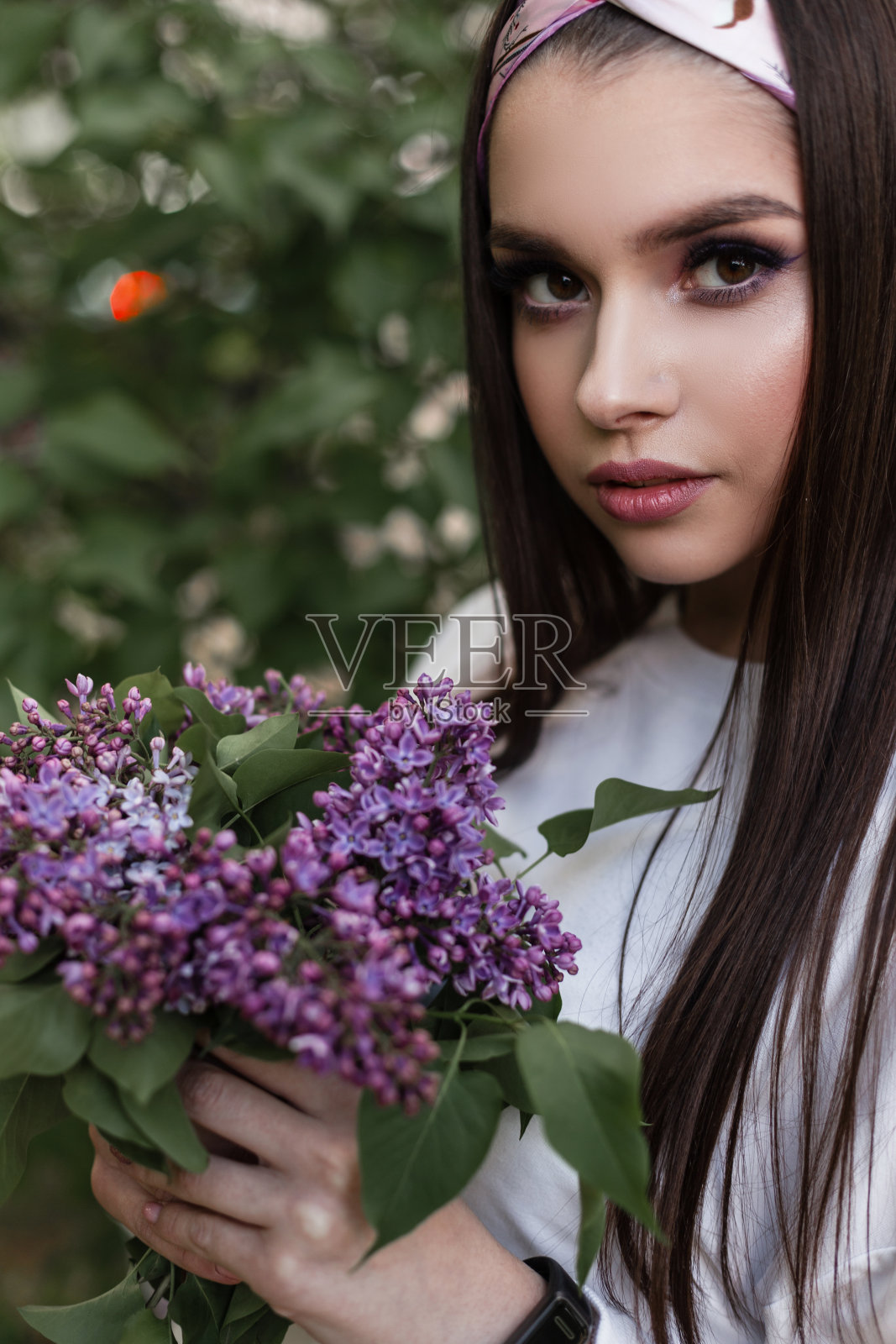 美丽的女人在迷人的头巾在白色时尚的穿着站在惊人的彩色花束在绿色的树叶在公园。温柔可爱的女孩喜欢春天和花园里的丁香花。春画像夫人。照片摄影图片