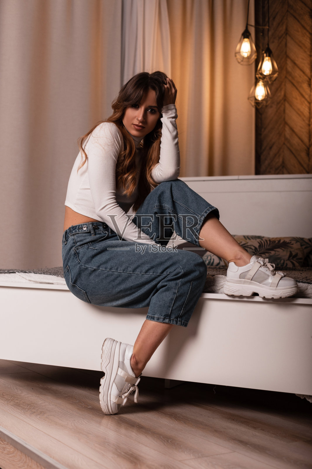 美丽奢华的红发年轻女子，穿着时尚的休闲服，穿着时尚的白色运动鞋，在房间里舒适柔软的床上放松。一个迷人的性感女孩在卧室摆姿势的时尚模特。时尚女士照片摄影图片