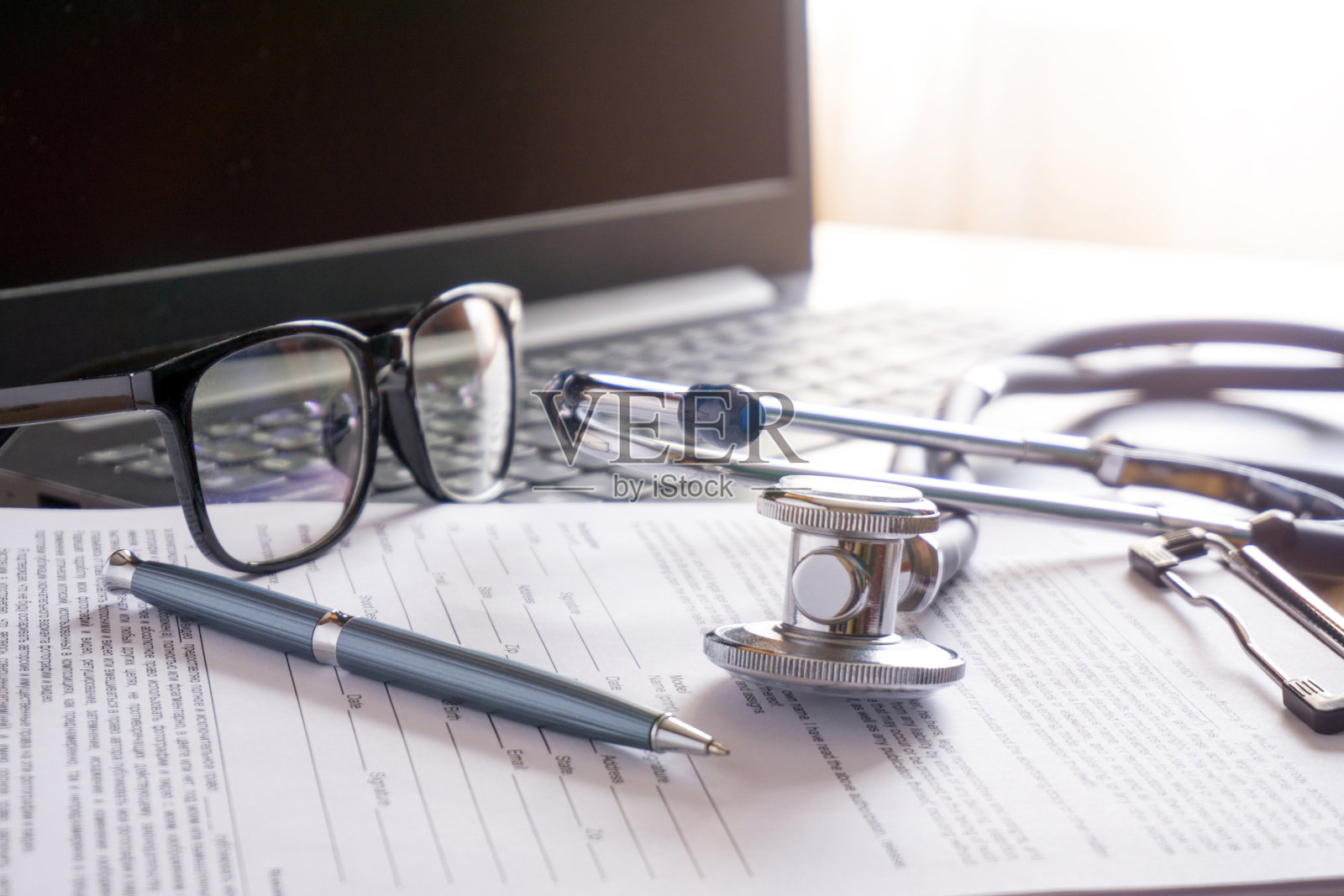 听诊器眼镜和一支写有文件的笔放在笔记本电脑旁边照片摄影图片