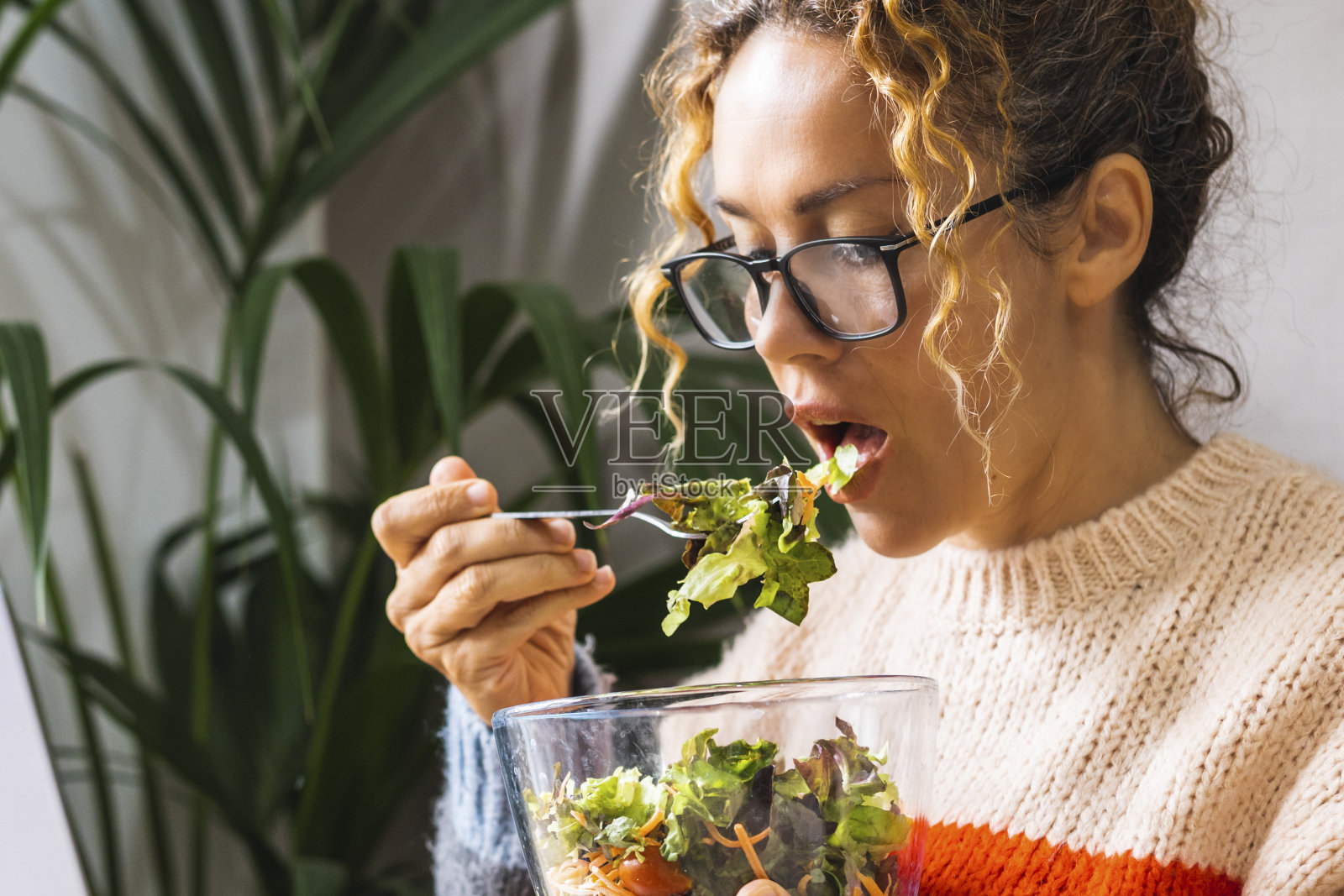 正在节食的女人一边在家里用笔记本电脑看在线节目，一边用透明的碗吃新鲜的沙拉。年轻的企业家忙于新的商业概念生活方式在线。午休时间女士照片摄影图片