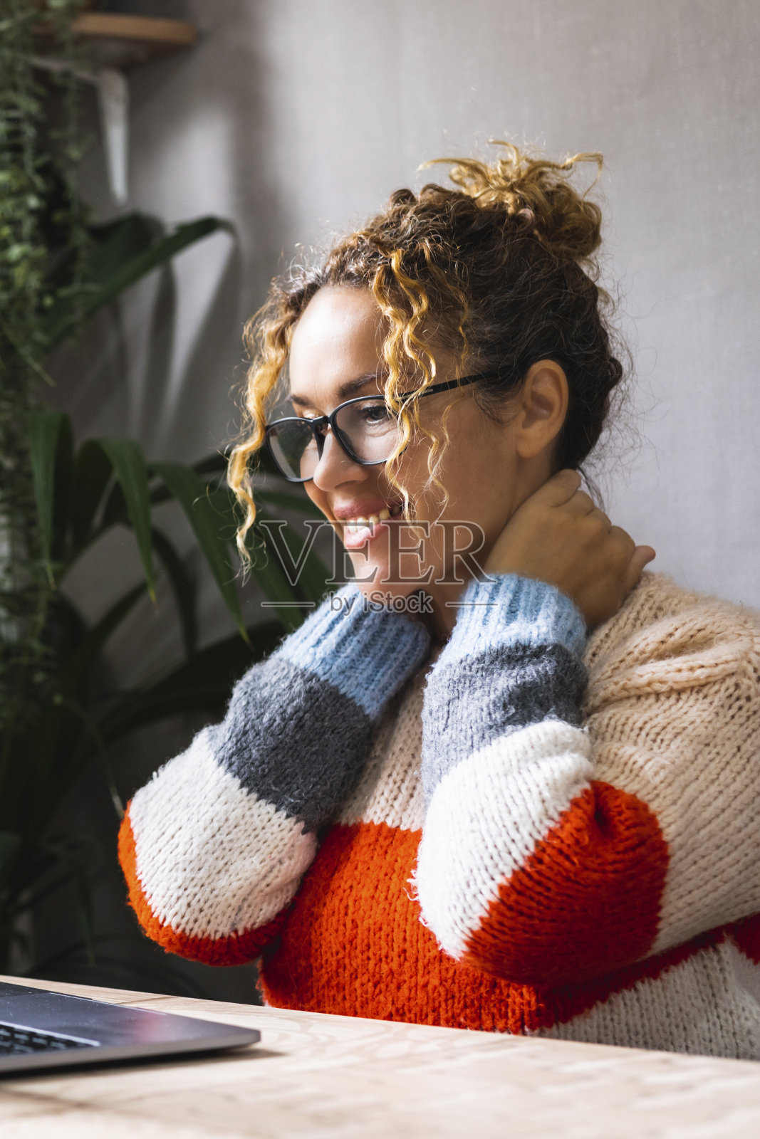 年轻的企业家正在休息，微笑着摸着脖子，看着笔记本电脑屏幕上的内容。在线现代工作。人们用电脑在家里的桌子上独自上网快乐照片摄影图片