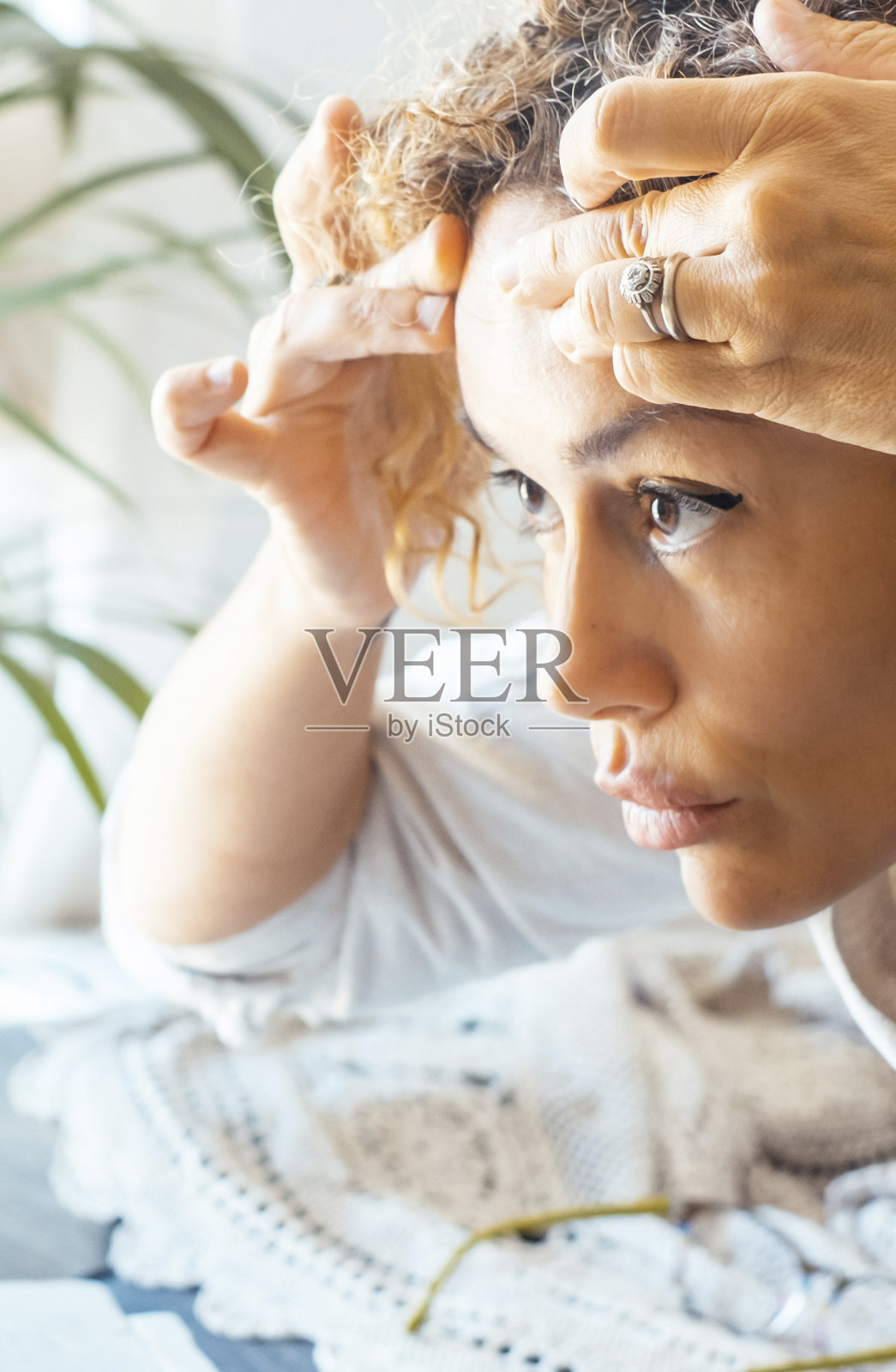 一位成年女士在家里摸着前面的皮肤检查年龄的皱纹。在桌子上的一面小镜子前。老年妇女的概念。女性担心衰老和皮肤护理。侧视图照片摄影图片