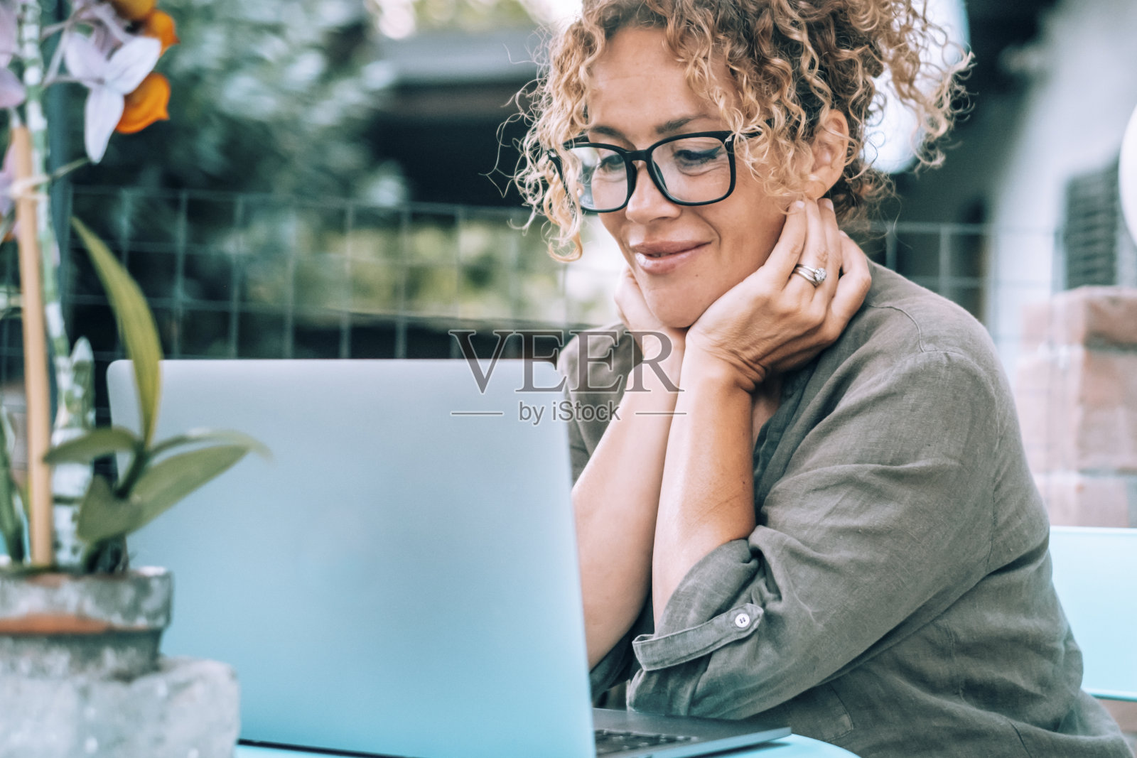 恬静的女子在户外家中使用电脑，在桌边享受户外科技在线休闲活动。现代女性看着笔记本电脑，微笑着。人们戴眼镜，放松生活方式照片摄影图片