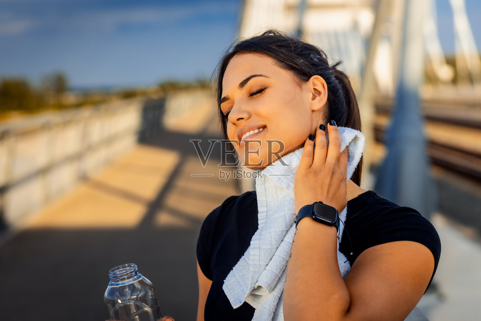 穿着黑色运动服的年轻女子在跑步后休息和喝水。照片摄影图片
