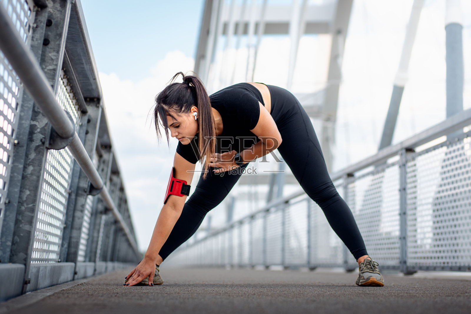穿着黑色运动服的年轻健身女性准备在桥牌上跑步伸展肌肉。照片摄影图片
