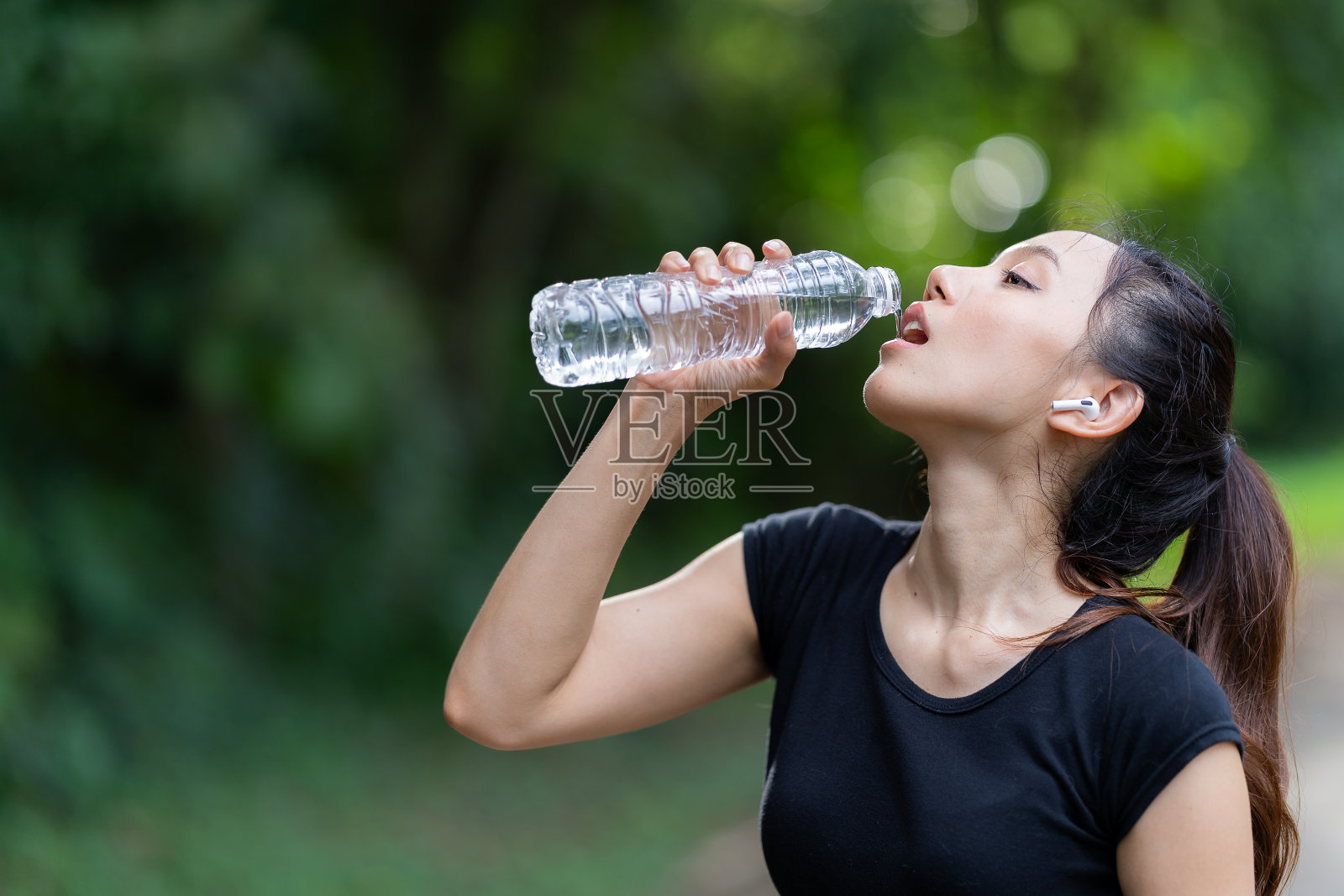 一个年轻的女模特穿着运动服在锻炼前做准备和喝水。在开始锻炼之前，打开一瓶干净的水让自己清醒一下。照片摄影图片