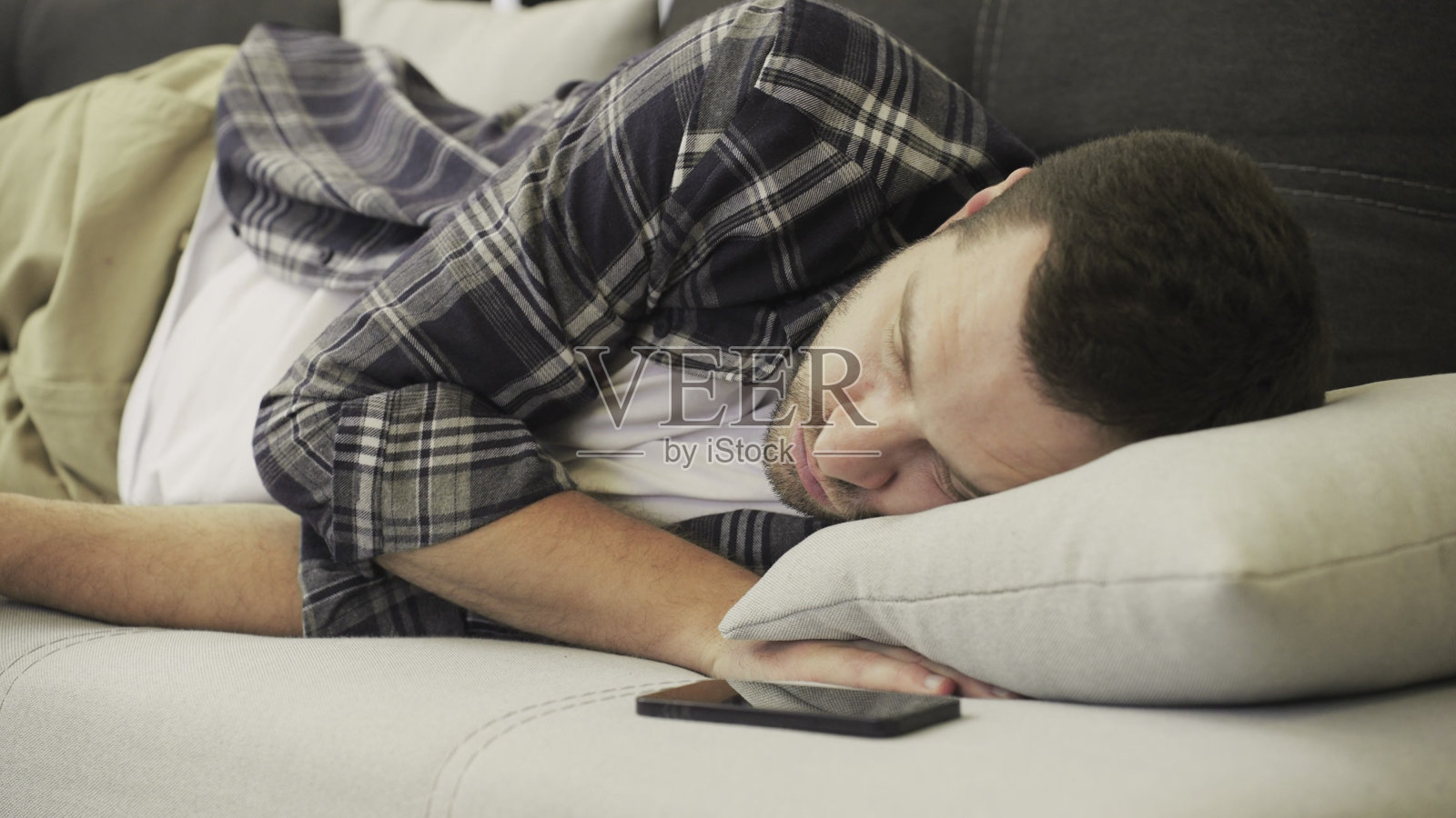 年轻人躺在沙发上，脸朝下，工作一天后很累。慢动作照片摄影图片