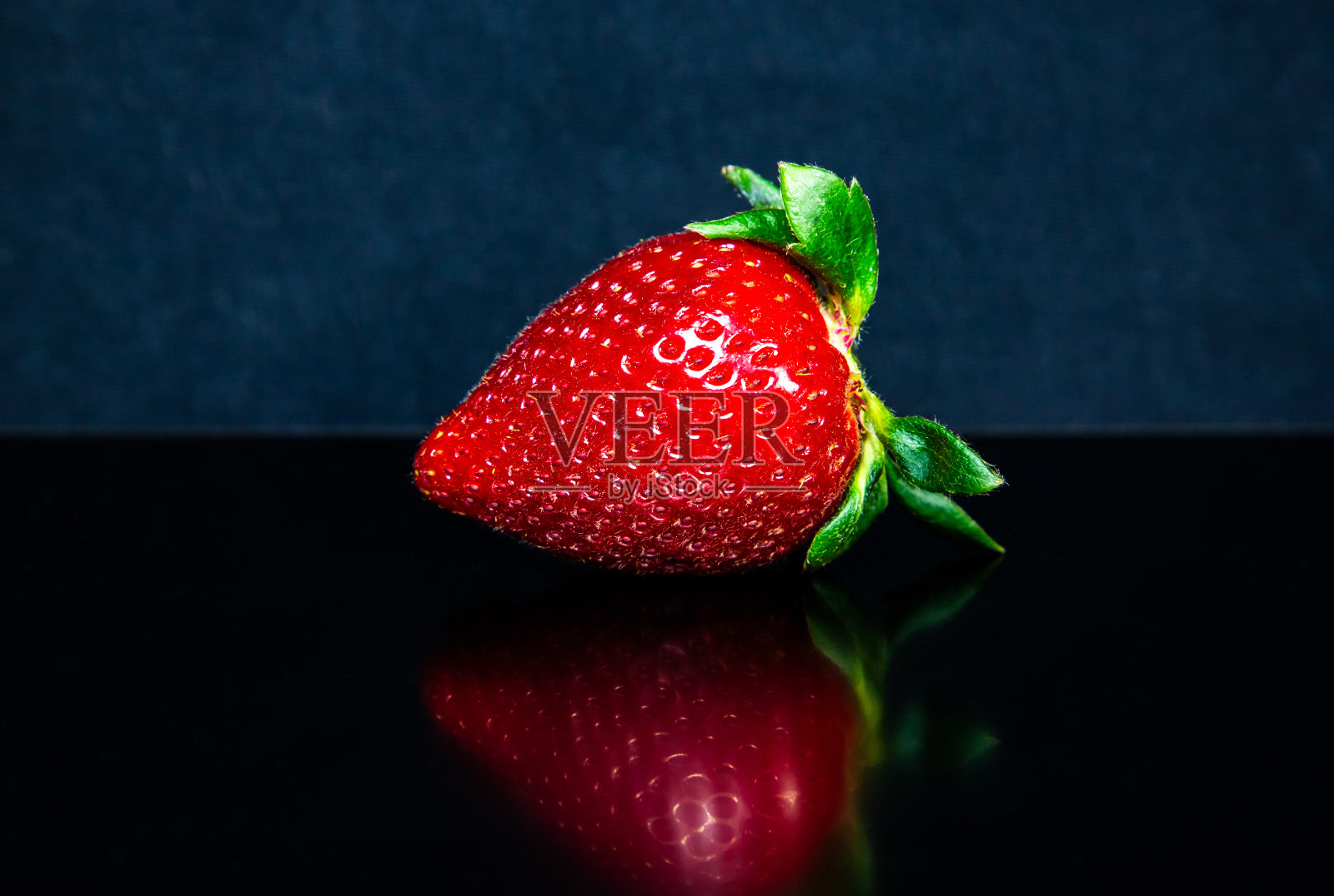一个草莓放在桌子上，背景是黑色的照片摄影图片