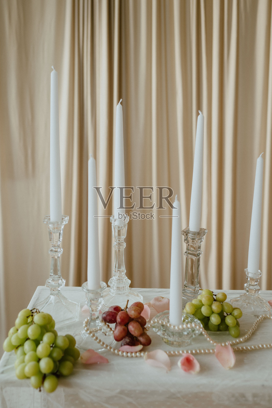 烛台和亮着葡萄、珍珠和粉红玫瑰花瓣的白蜡烛。照片摄影图片