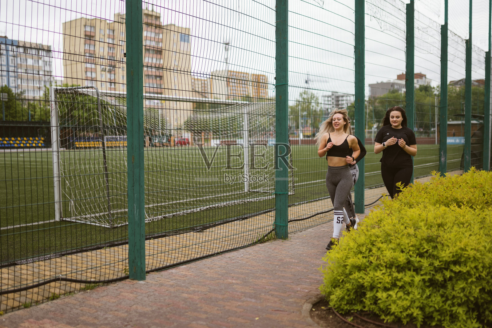 一名妇女在教练的陪同下沿着铺好的道路经过足球场照片摄影图片