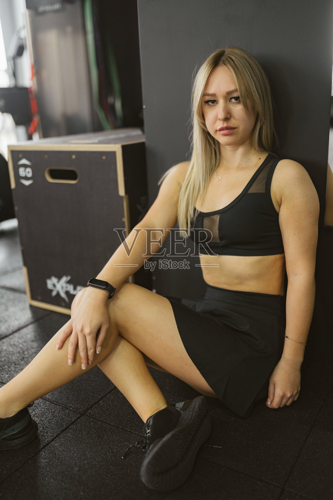 穿着黑色运动胸罩的年轻女子坐在健身房的地板上照片摄影图片