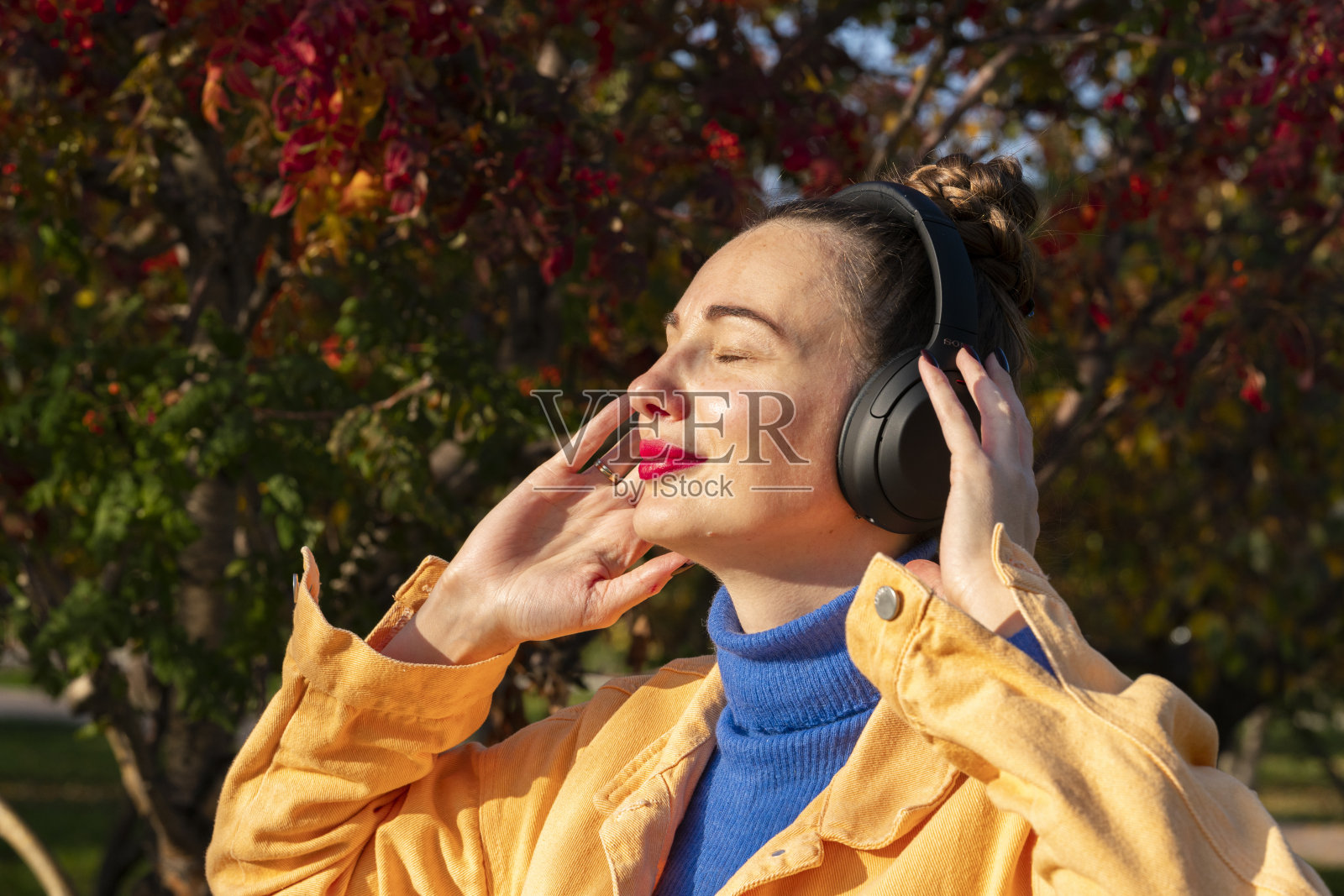 一个戴着耳机的年轻女子在秋天的公园里散步，听着音乐照片摄影图片