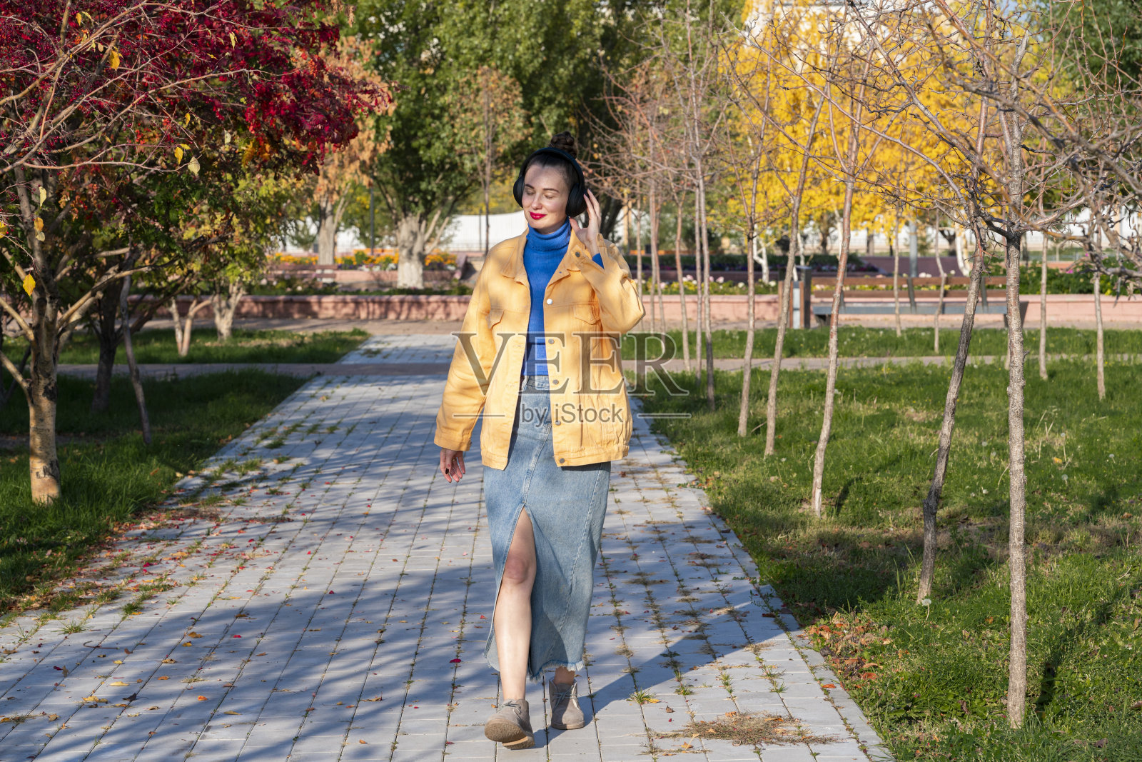 一个戴着耳机的年轻女子在秋天的公园里散步，听着音乐照片摄影图片