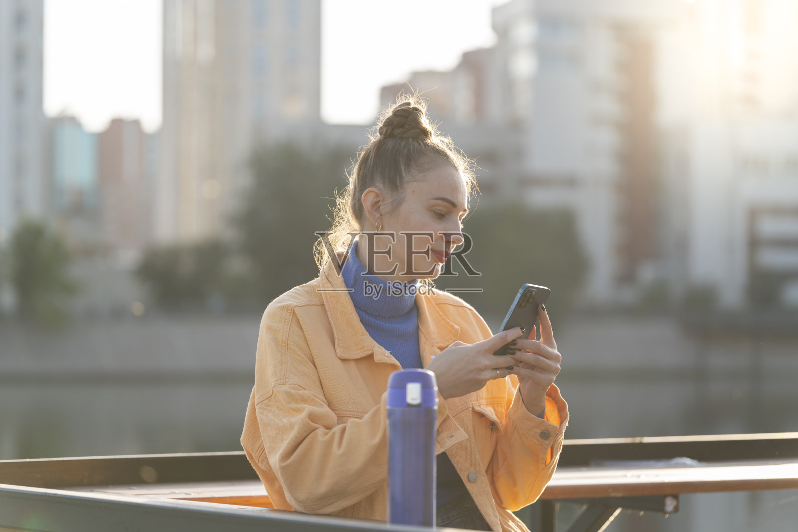 秋天，一名年轻女子在街上手持智能手机。照片摄影图片
