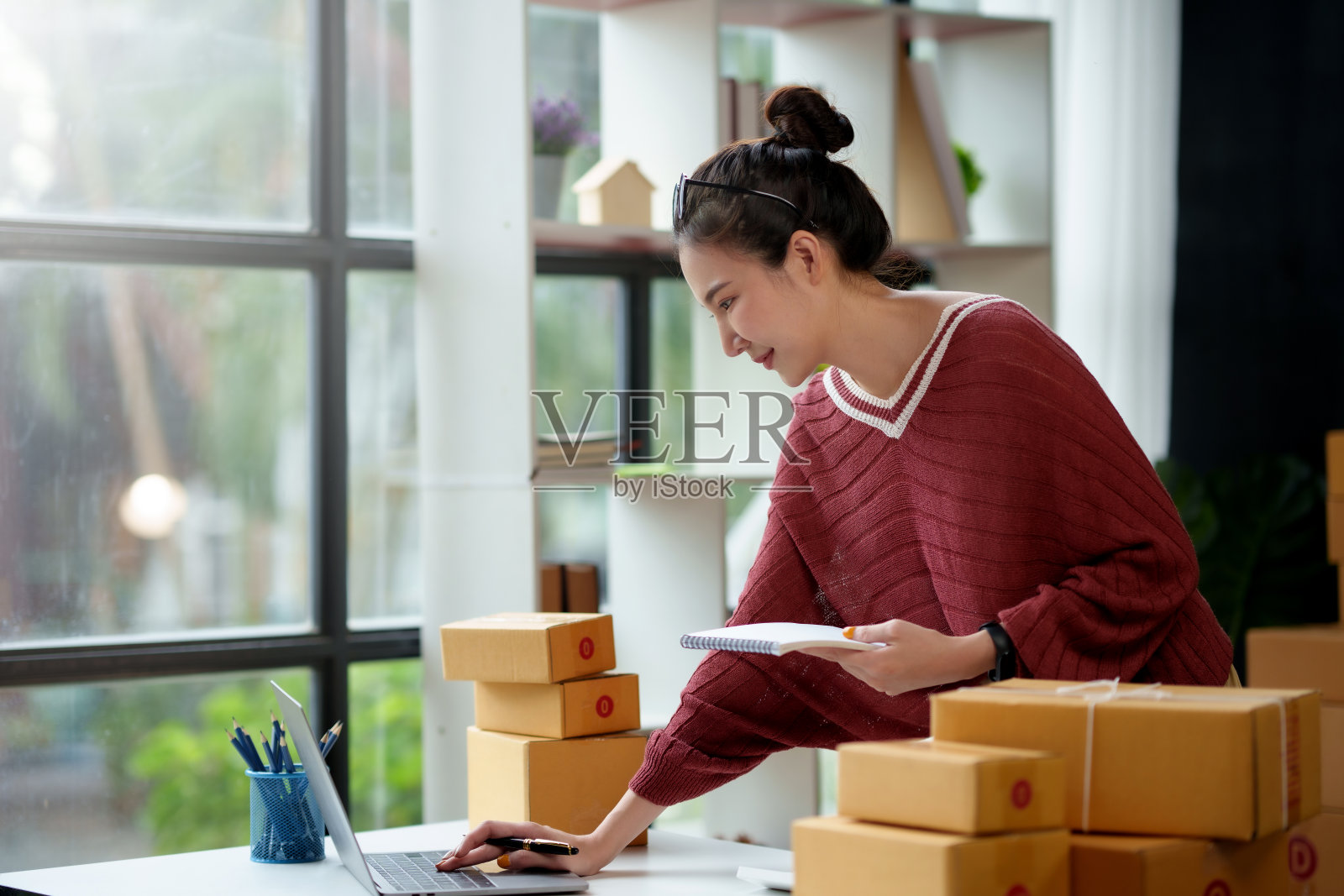 一名年轻的亚洲在线企业主微笑着，用笔记本电脑准备包裹箱和检查在线订单，以便将产品送到客户手中。照片摄影图片