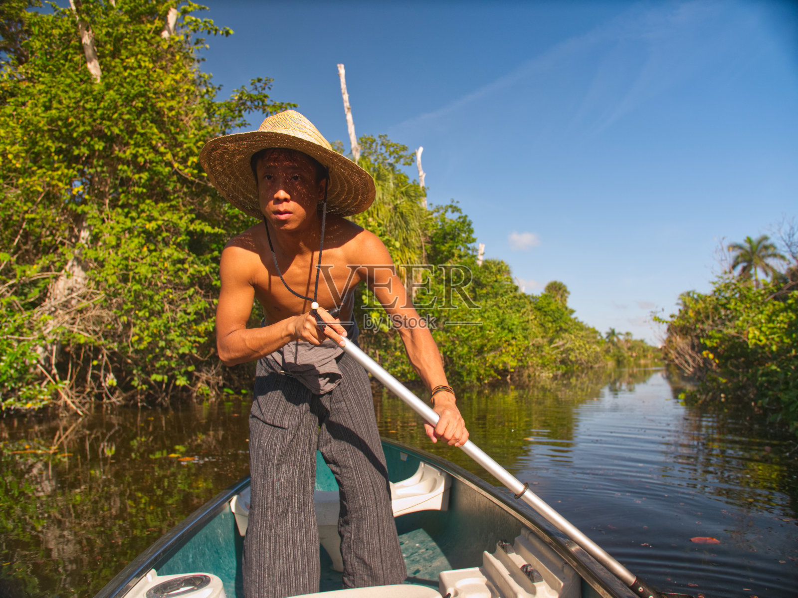 戴草帽的亚洲男子划着独木舟顺流而下照片摄影图片