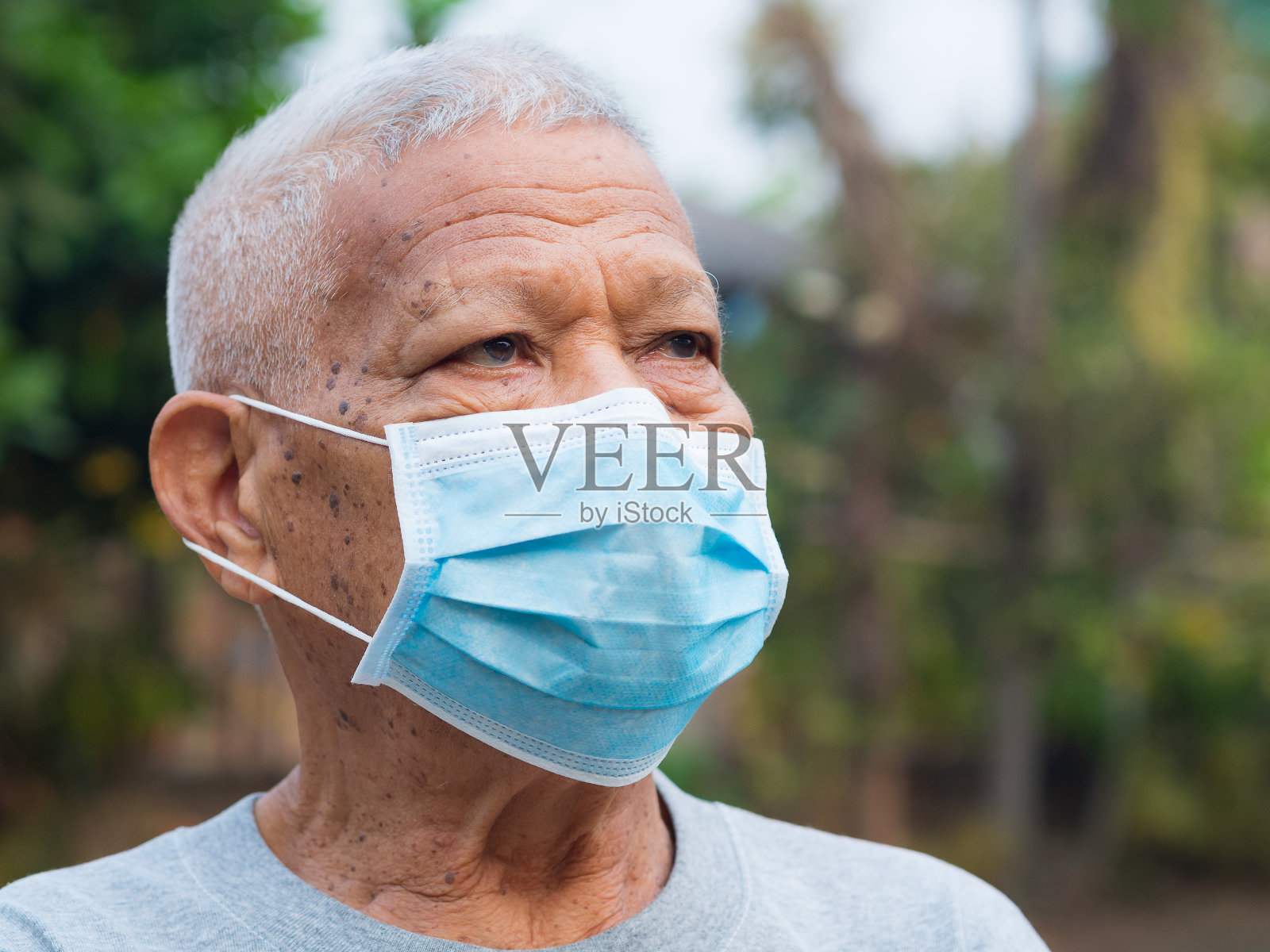 一位戴着口罩站在花园里的亚洲老人的画像。照片摄影图片