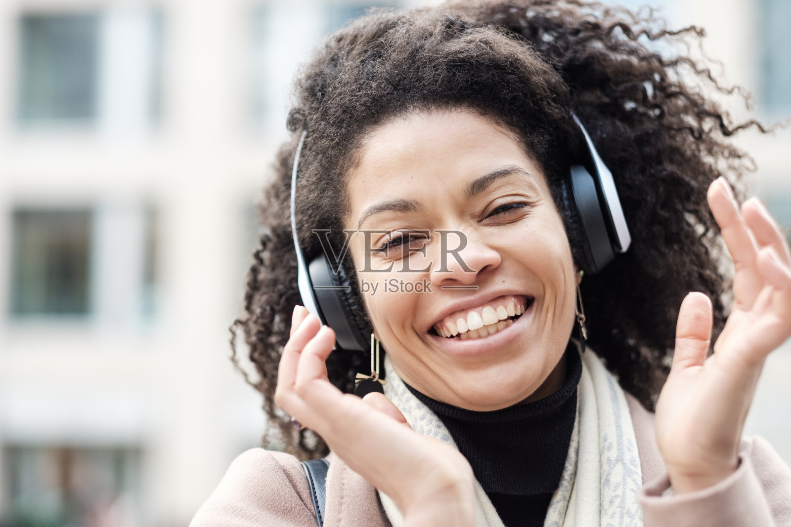 快乐的黑人妇女戴着耳机在户外欣赏音乐的大头照。照片摄影图片