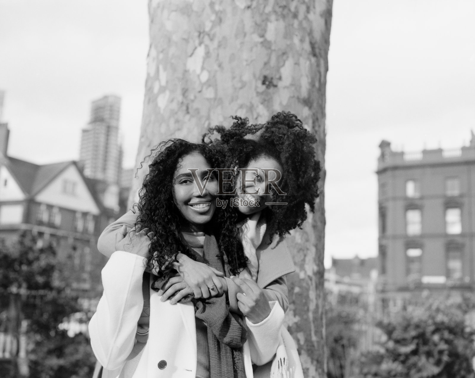 两个女性朋友在树前互相拥抱的模拟肖像。照片摄影图片