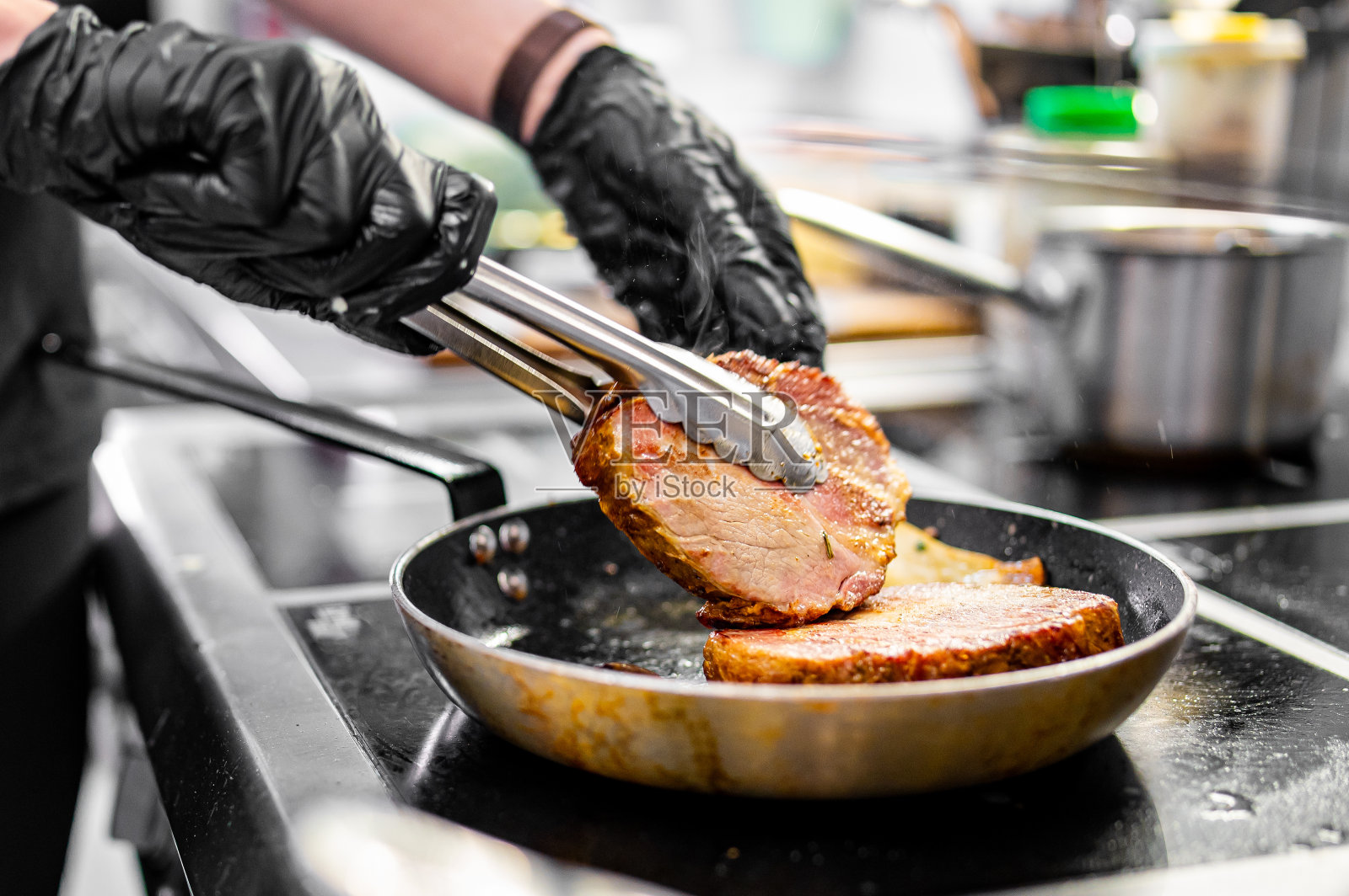 专业厨师在餐厅厨房的炉子上用煎锅烹饪牛排照片摄影图片