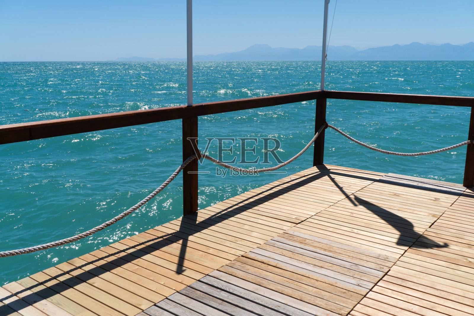 有柱子和绳子的木制码头，海水闪闪发光。蓝色大海背景的木制码头。照片摄影图片