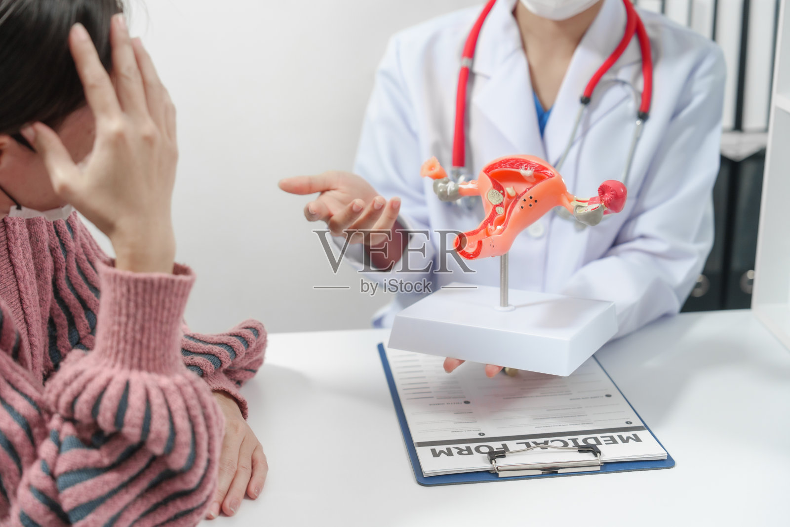 女医生用安慰的手势安抚病人，桌子上放着女性系统的模型，可能会讨论月经、宫颈癌、不孕症或绝育。照片摄影图片