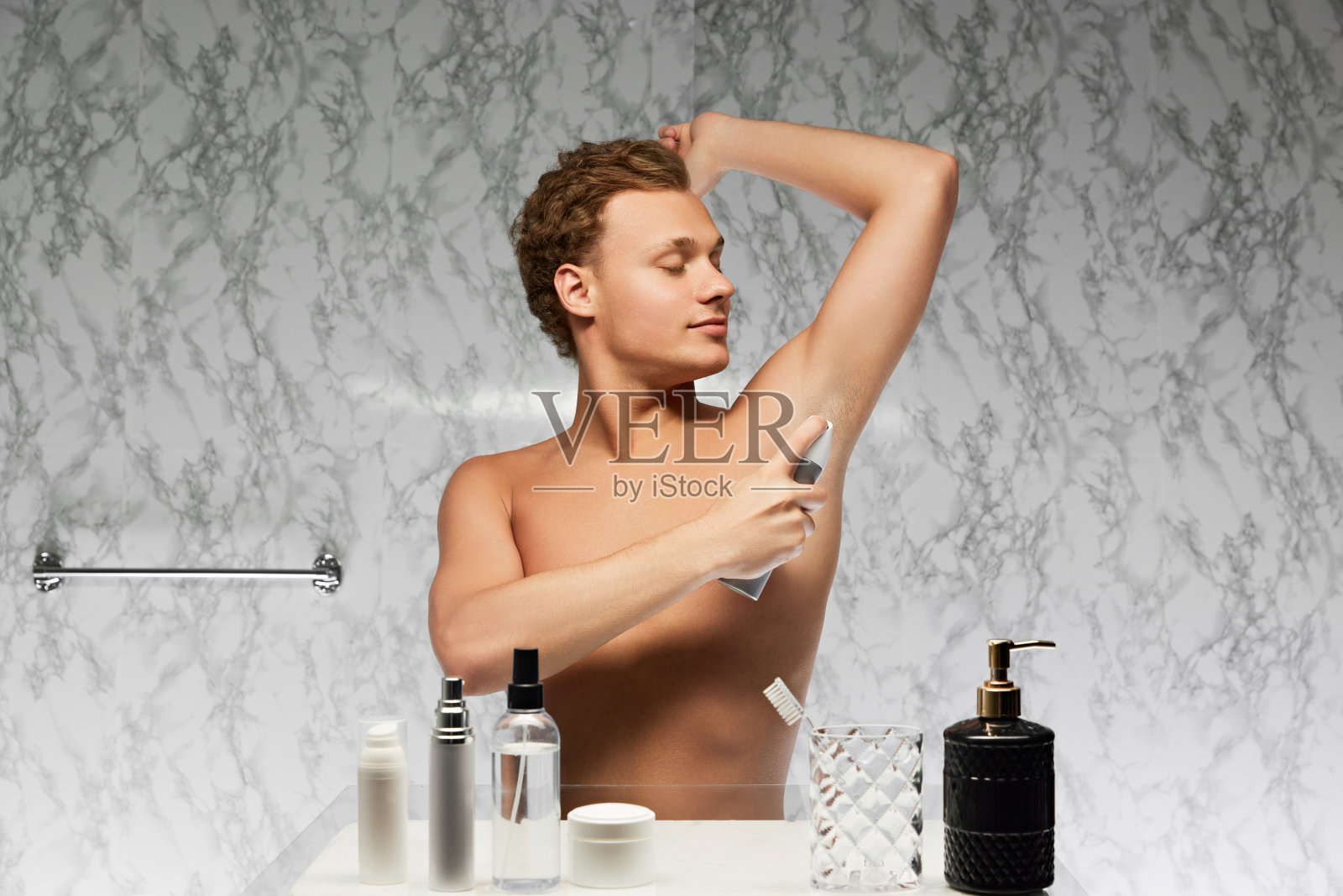 赤裸上身的年轻男子将汗液举起手，贴在浴室大理石墙壁的腋下部位。照片摄影图片