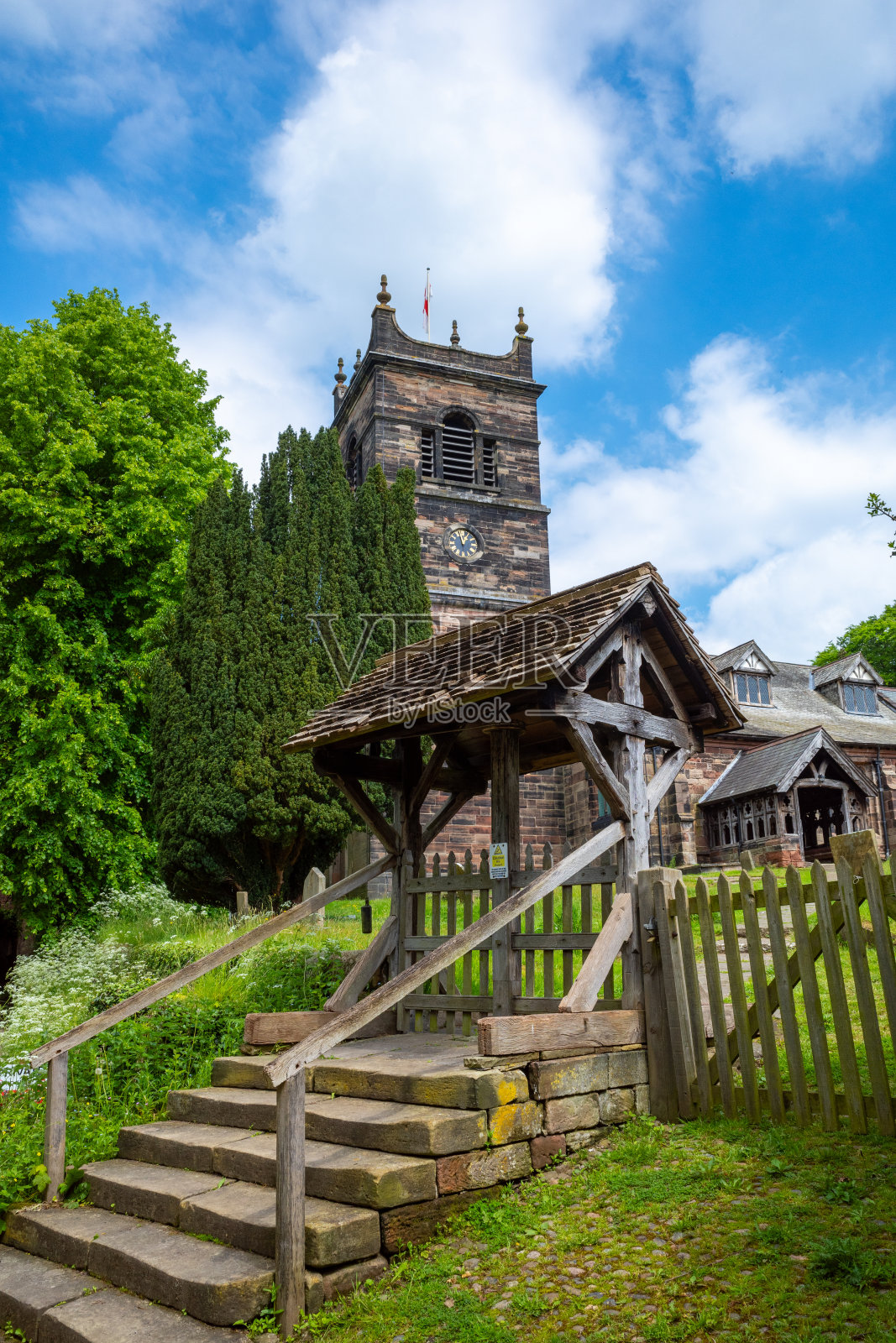 历史悠久的石头教堂，木质的教堂门和钟楼，郁郁葱葱的绿色植物和明亮的蓝天照片摄影图片