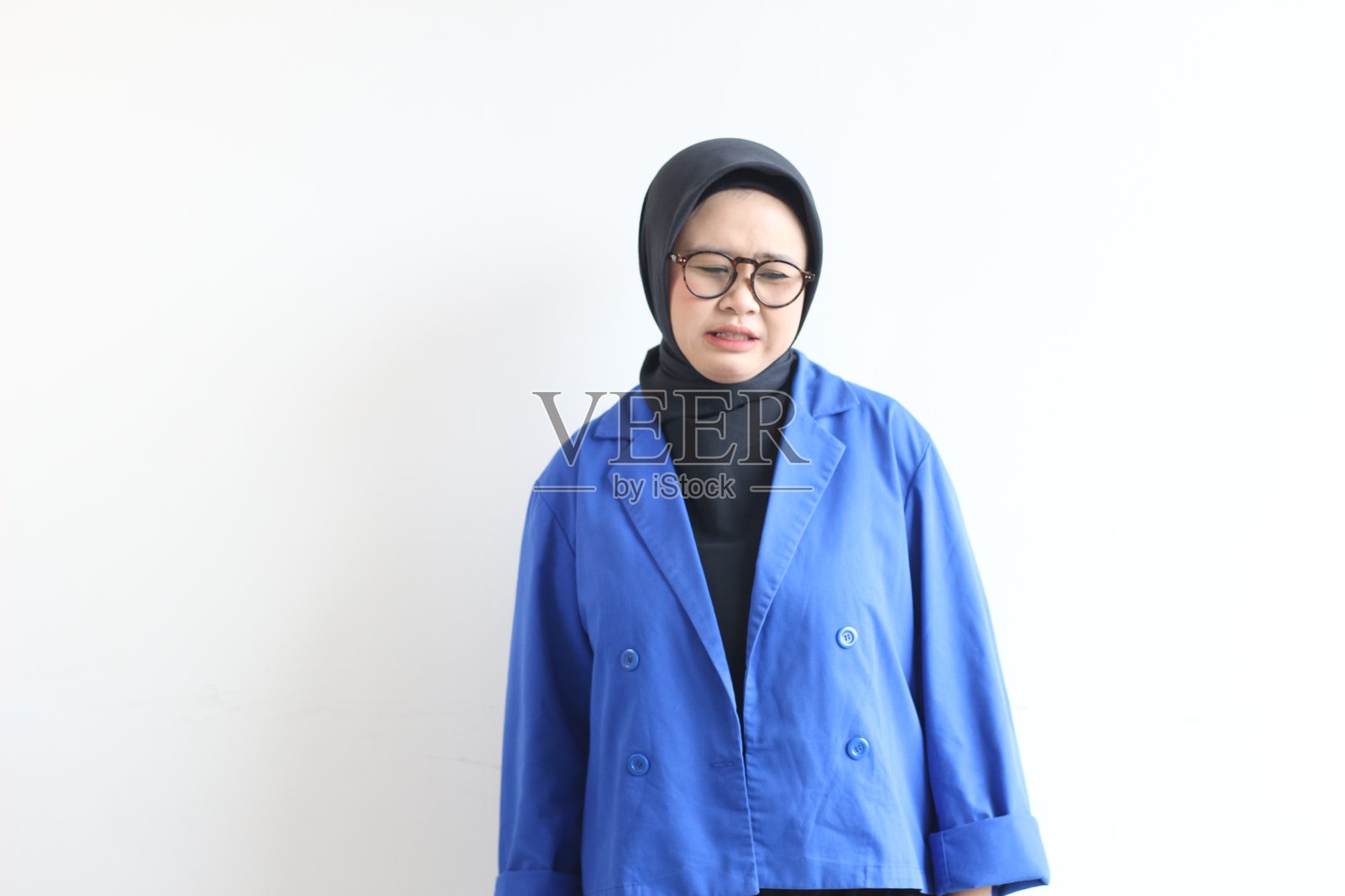 年轻漂亮的亚洲穆斯林女人，戴着眼镜，穿着蓝色西装，脸上带着厌恶的表情照片摄影图片