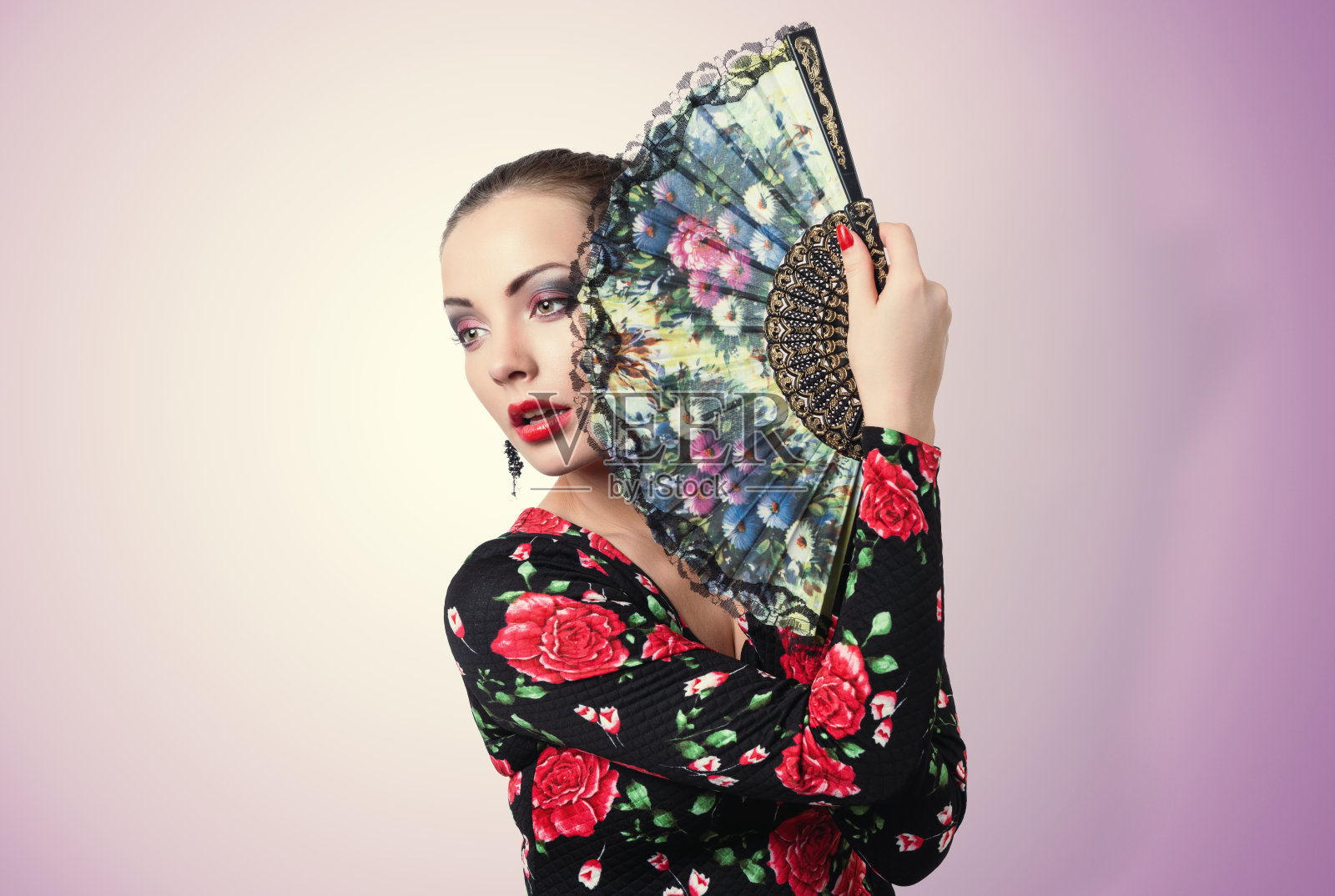 这位快乐的黑发女郎身穿黑色连衣裙，上面点缀着弗拉门戈风格的花朵，手里拿着一把敞开的扇子，背景是黄粉色照片摄影图片