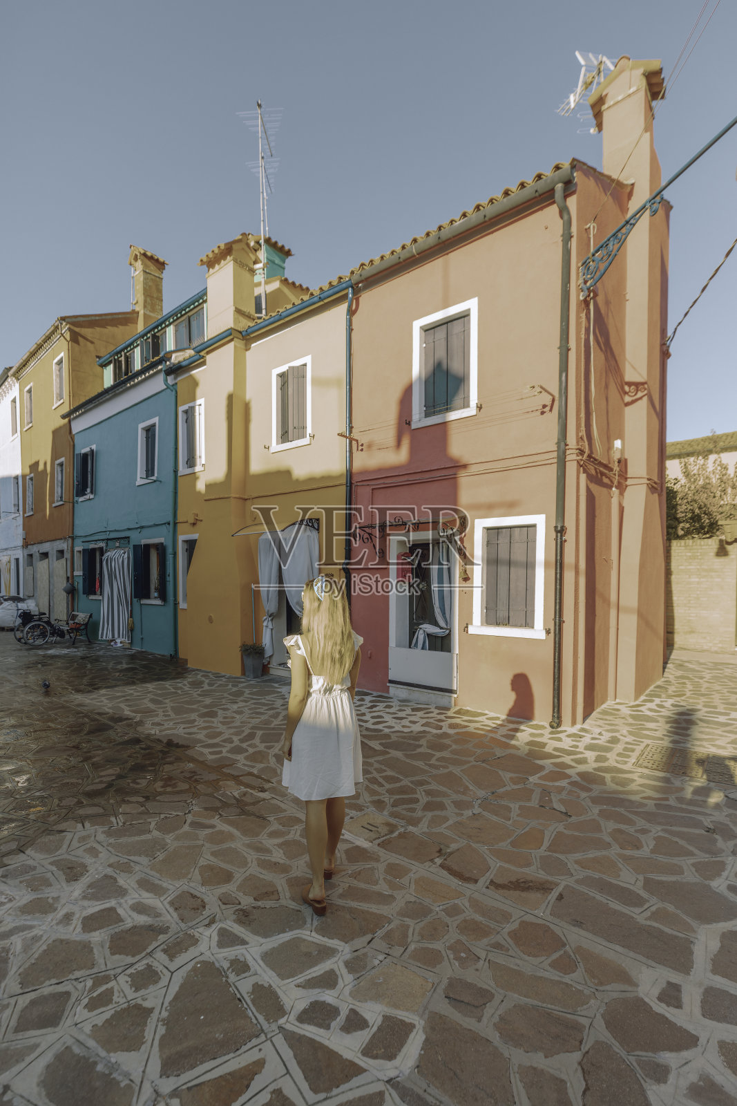 在意大利威尼斯的布拉诺，穿着白色连衣裙的年轻女游客在运河边享受阳光明媚的一天照片摄影图片