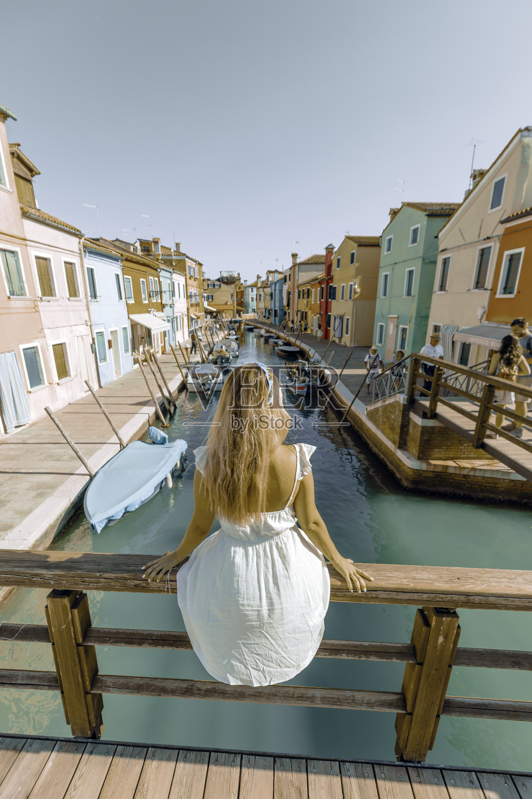 在意大利威尼斯的布拉诺，穿着白色连衣裙的年轻女游客在运河边享受阳光明媚的一天照片摄影图片