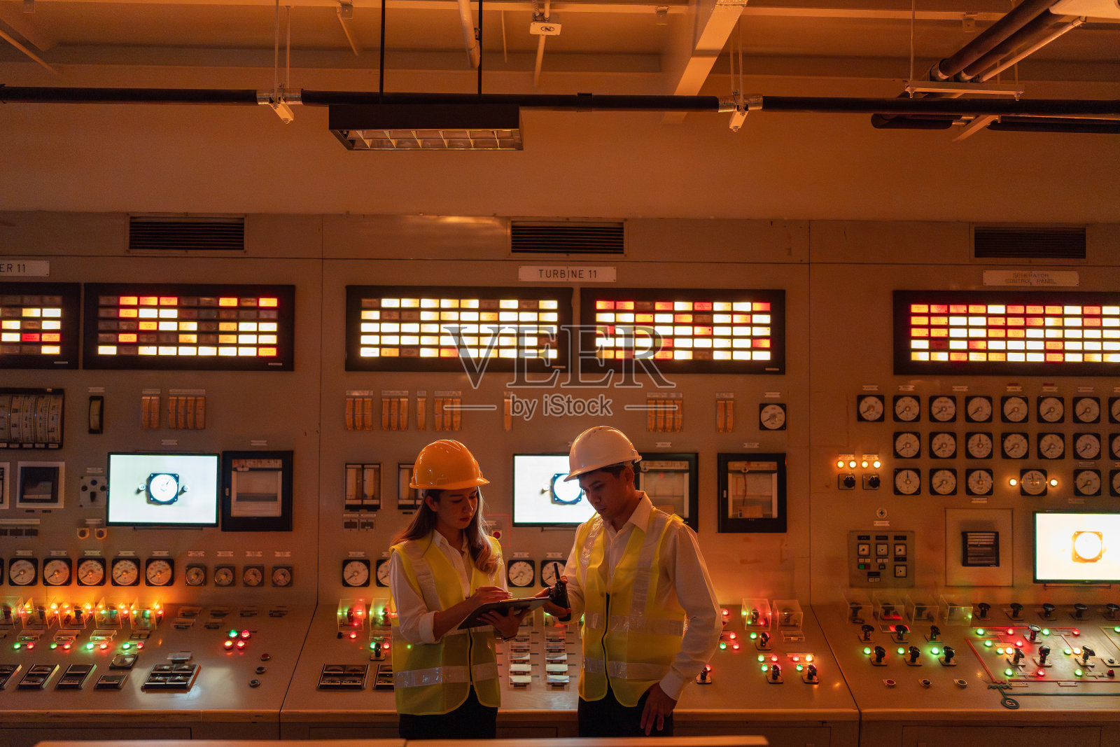 亚裔男女工程师使用笔记本电脑和对讲机查看系统。戴着安全帽，穿着背心，你在一家大型发电厂，为全球工业出口能源。照片摄影图片