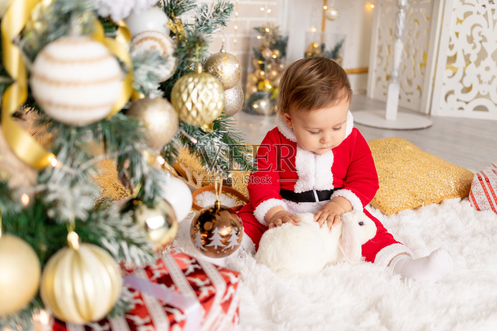 一个穿着圣诞老人服装的孩子和一只兔子坐在圣诞树前，这是新年和圣诞节的概念照片摄影图片