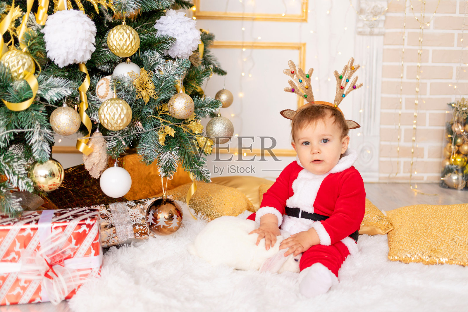 一个穿着圣诞老人服装的孩子和一只兔子坐在圣诞树前，这是新年和圣诞节的概念照片摄影图片