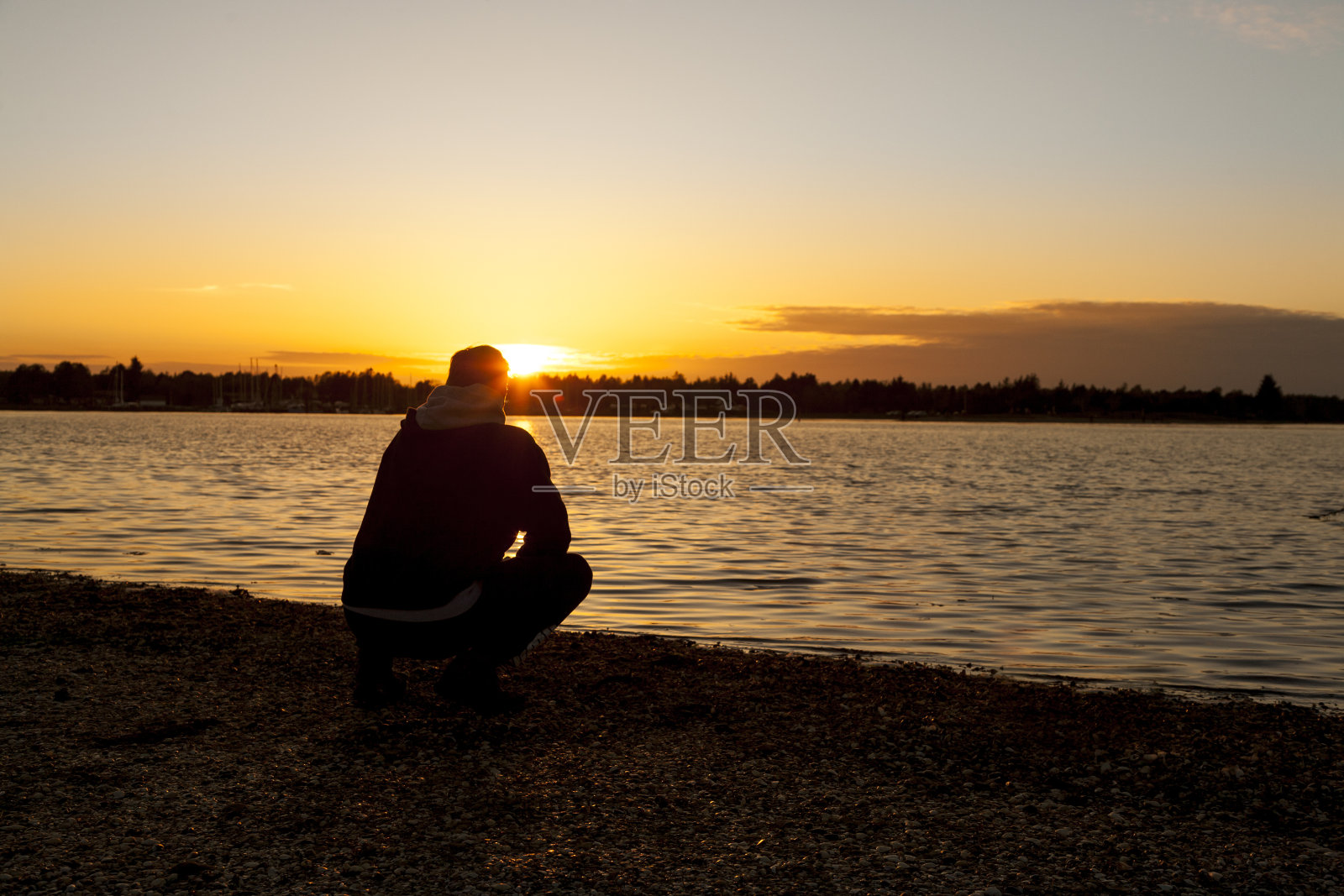 一个中年男子坐在沙滩上看日出的剪影照片摄影图片