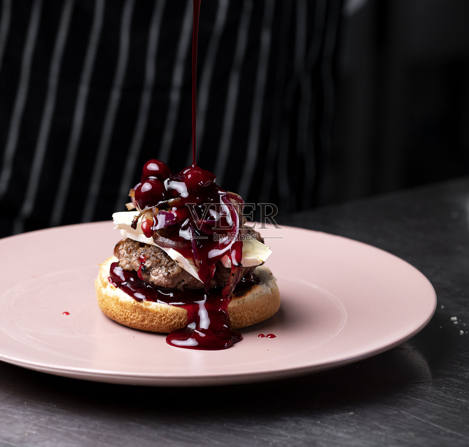 厨师用肉饼、樱桃、布里奶酪和焦糖洋葱制作了一个汉堡。照片摄影图片