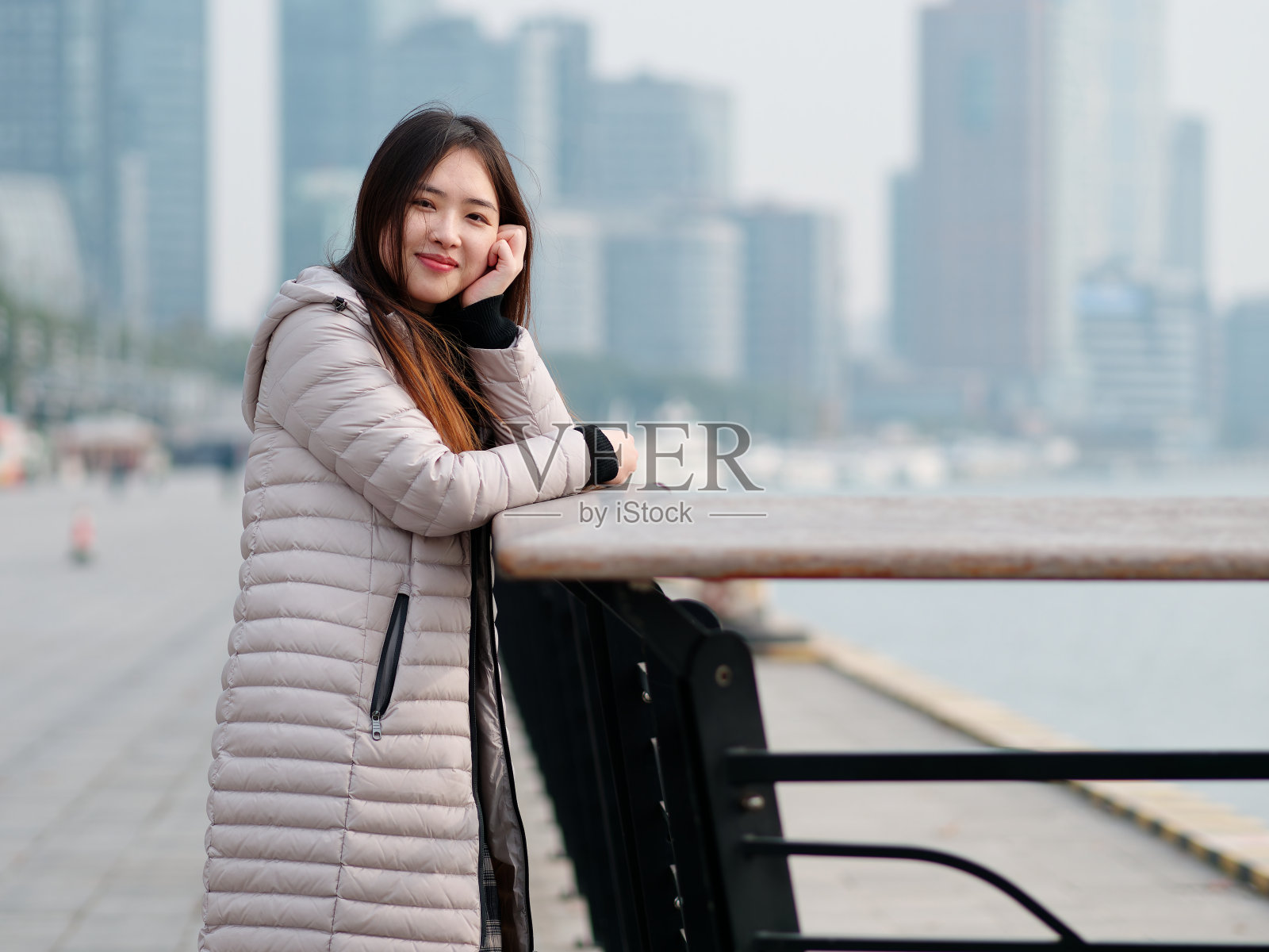 在阳光明媚的日子里，穿着长羽绒服的中国女孩的肖像与模糊的城市背景。冬季户外时尚肖像魅力年轻的中国女士美丽时髦的女人，女性的生活方式。照片摄影图片