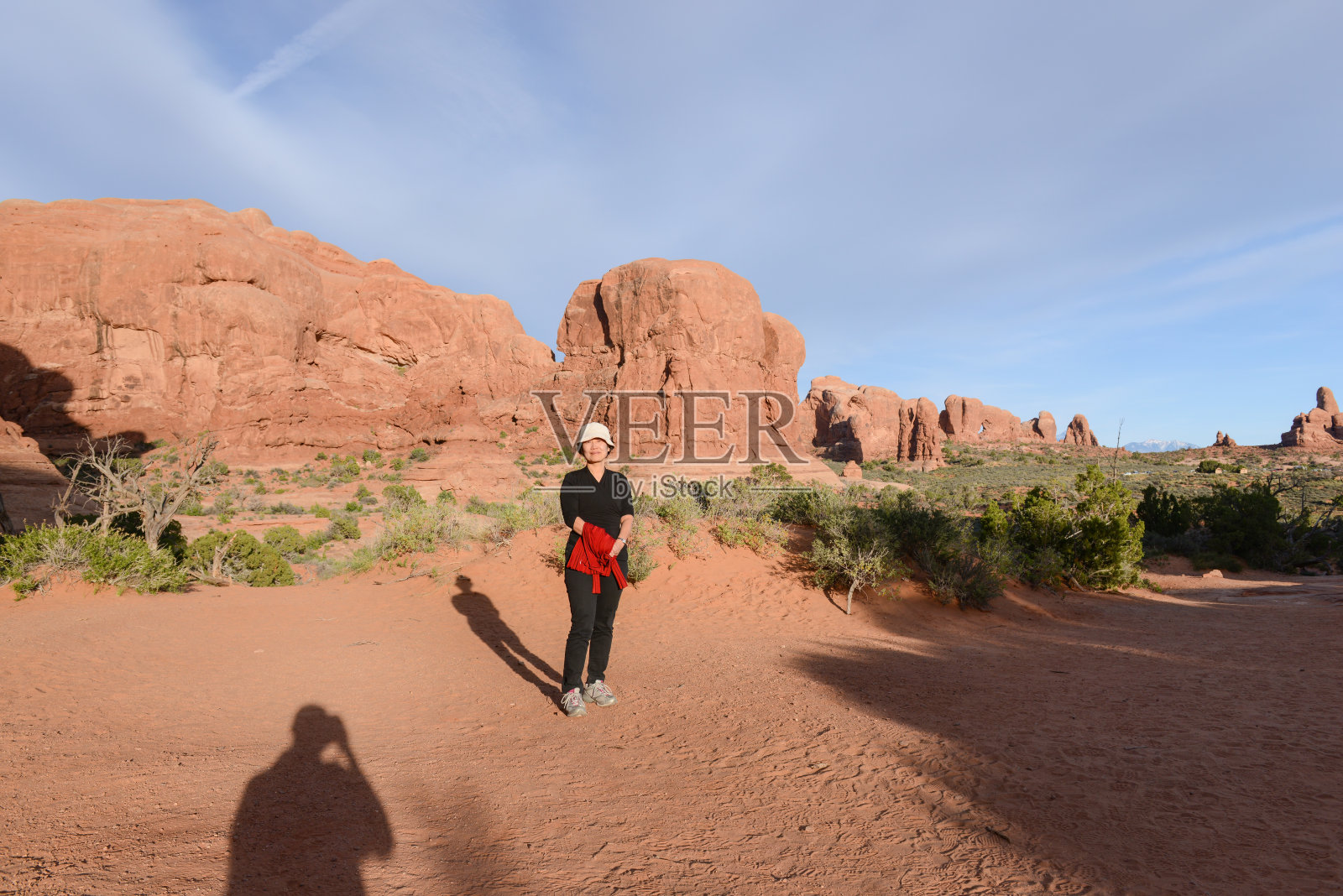 女游客摆姿势拍照。摄影师在红沙滩上的影子。拱门国家公园。犹他州。美国。照片摄影图片