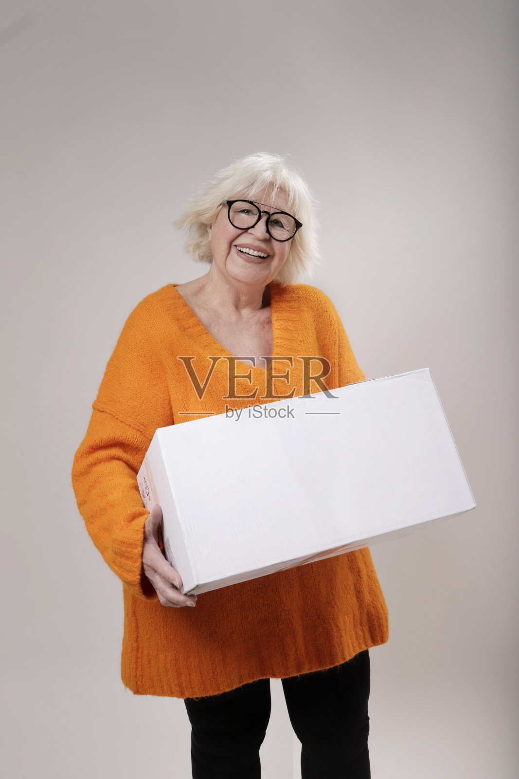 满脸笑容的大妈顾客在家里收邮包，开心的老婆婆捧着打开的纸板箱坐在客厅的沙发上，网购订购快递速递概念照片摄影图片