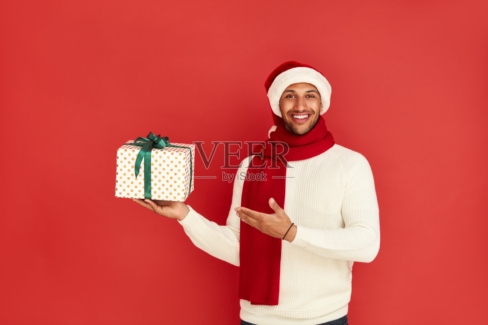 男子指着新年礼物。戴圣诞帽的人盯着礼品盒看照片摄影图片