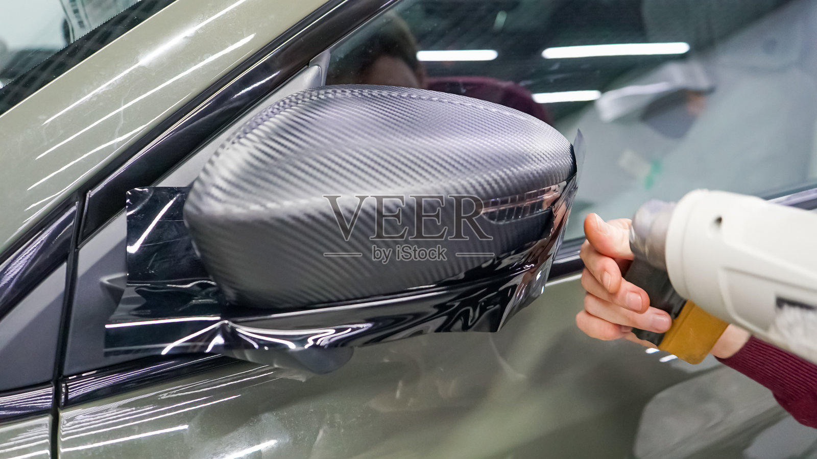 在侧镜上安装碳膜的过程。汽车包装特写。汽车包装。汽车包装专家将碳膜涂在汽车上。有选择性的重点。照片摄影图片
