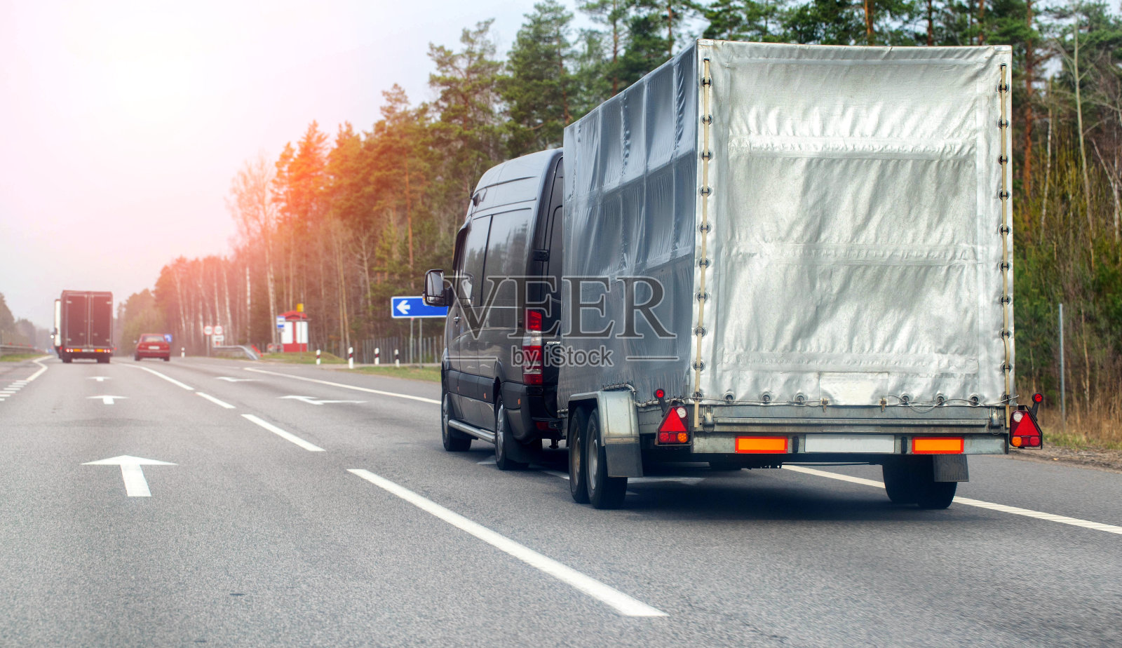 春天里，一辆载着行李的半挂车的小巴沿着一条沥青乡村公路行驶。租一辆带半挂车的小巴来装行李。文本的复制空间，日落照片摄影图片
