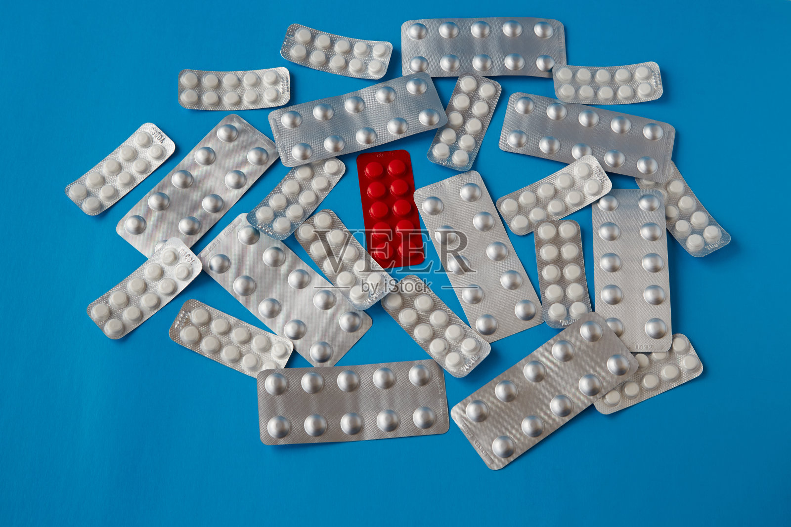 在蓝色背景的吸塑包装中，散落的白色药片中有红色药片。照片摄影图片