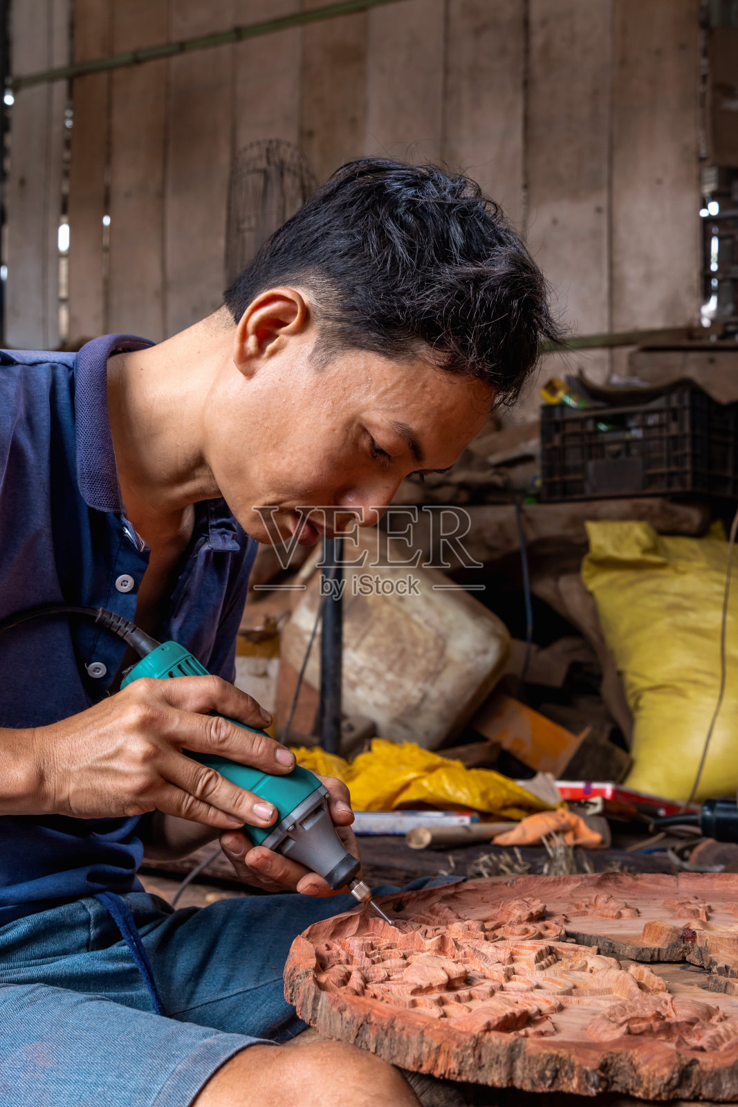 图为，在木工车间工作的越南男子正在用机器在木头上画画。照片摄影图片