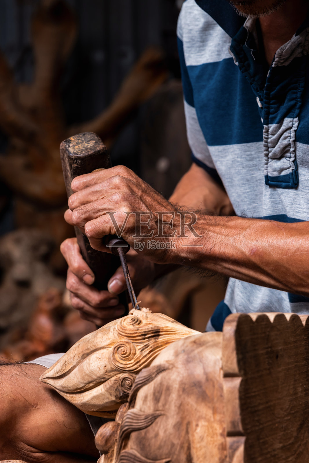 用锤子和凿子雕刻的手的垂直聚焦照片，木雕成龙的形状。照片摄影图片