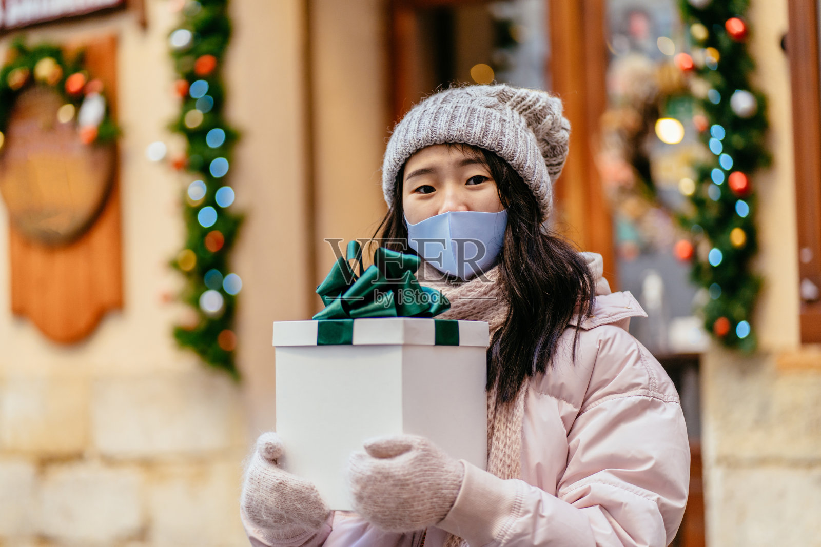 街道舒适的肖像友好的积极微笑的亚洲女士拿着礼盒绿色蝴蝶结在冬季城市与背景散景光。看镜头的韩国女性。关闭了。照片摄影图片